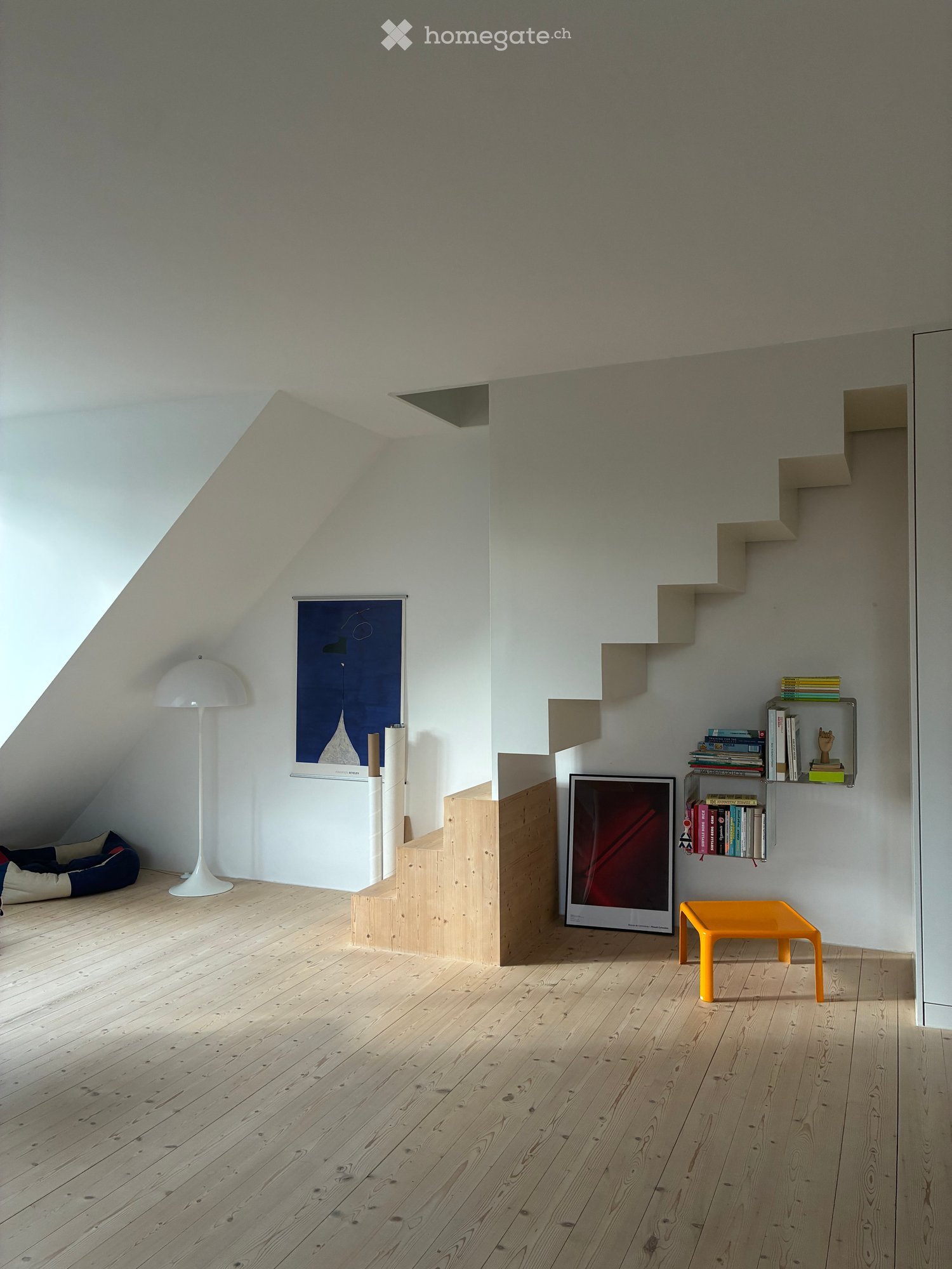 Attic room with wooden flooring, white walls, built-in shelves, a floor lamp, a small orange stool, and a dog bed in the corner.