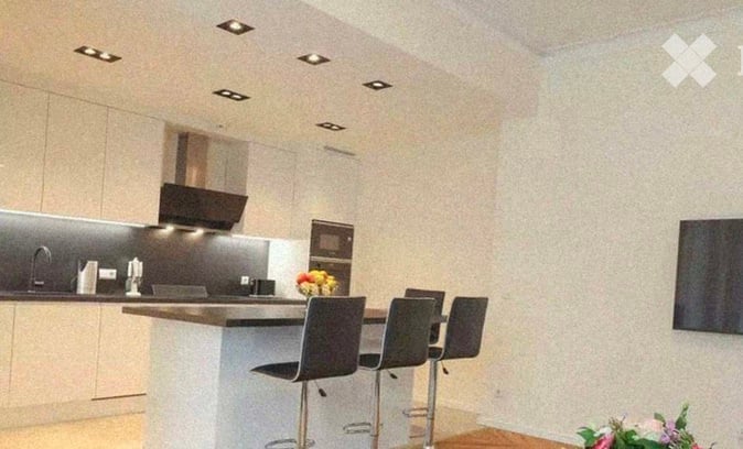 Modern kitchen with a central island, bar stools, sleek cabinetry, and a microwave. The space features recessed lighting and a minimalist design.