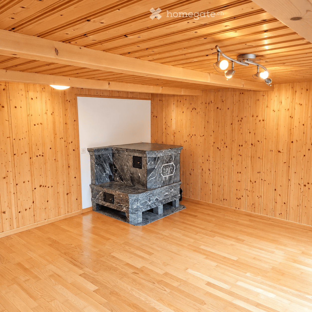 Empty room with wooden walls and ceiling, polished wooden floor, and a stone fireplace with a decorative plaque.