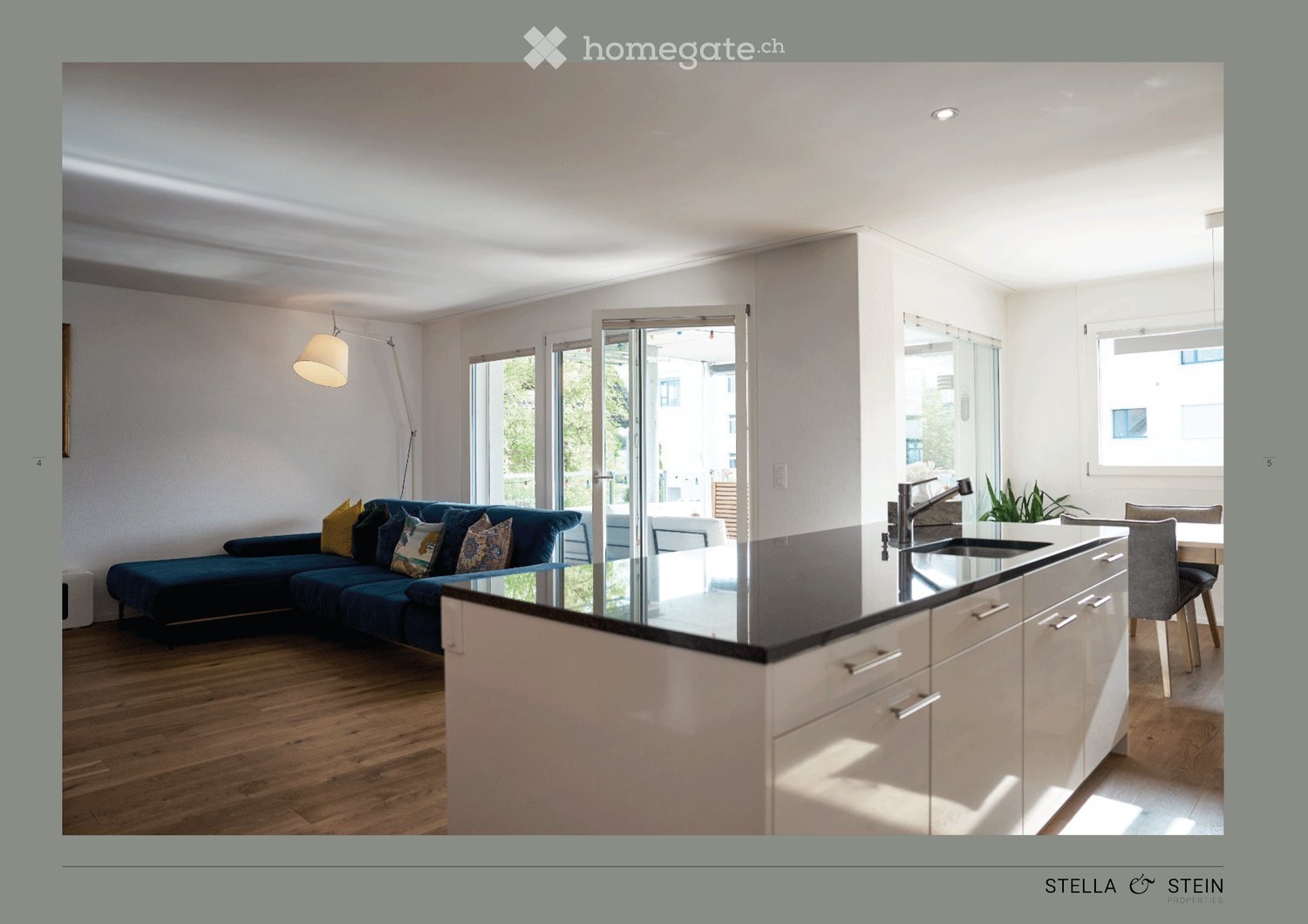 Open-plan living and kitchen area with a dark blue sofa, kitchen island, and modern fixtures.
