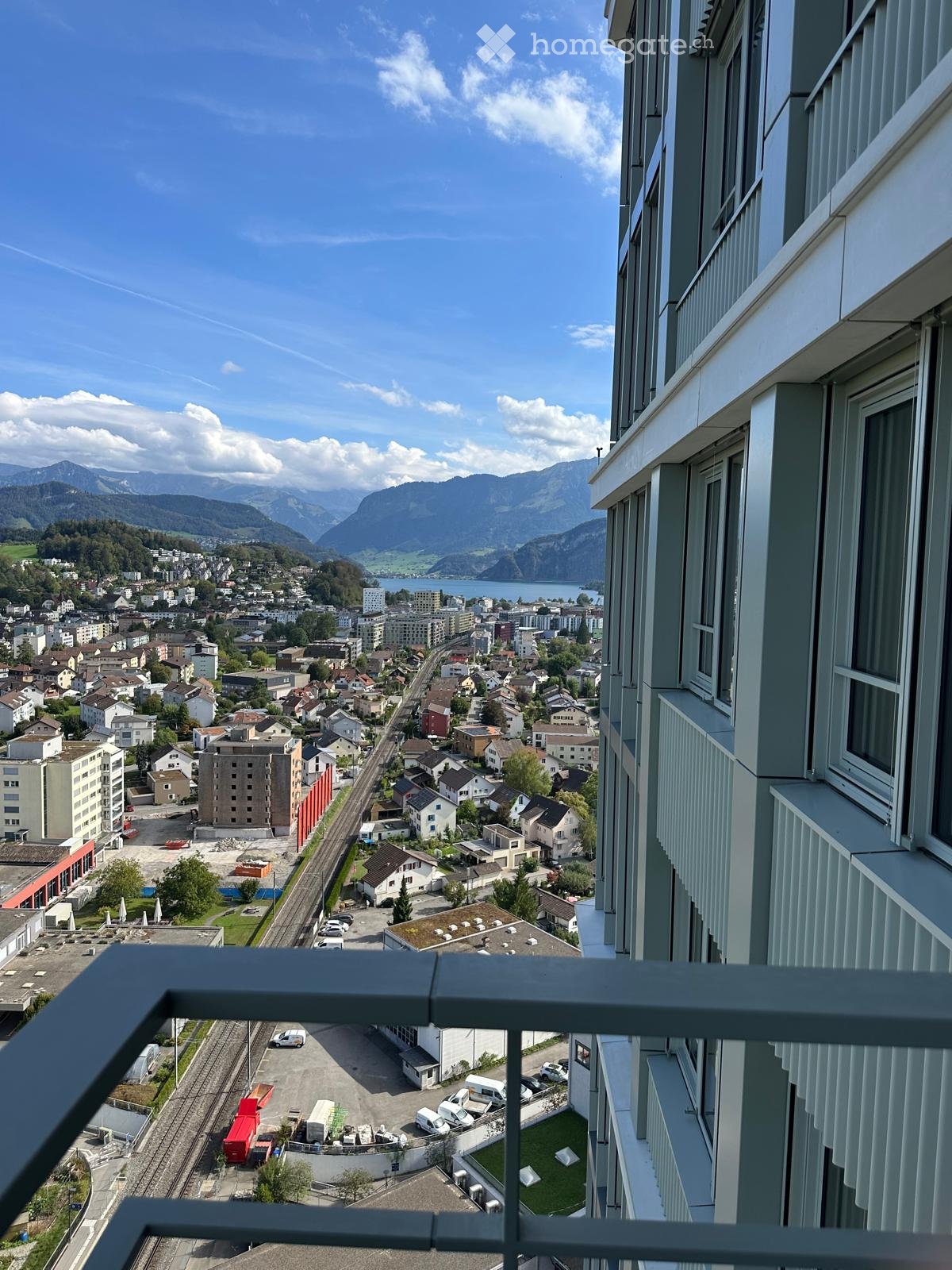 Balcony overlooking a town with houses, a lake, and mountains in the background.