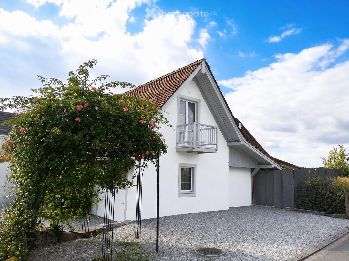 Single-story white house with a pitched roof, balcony, and surrounding greenery.