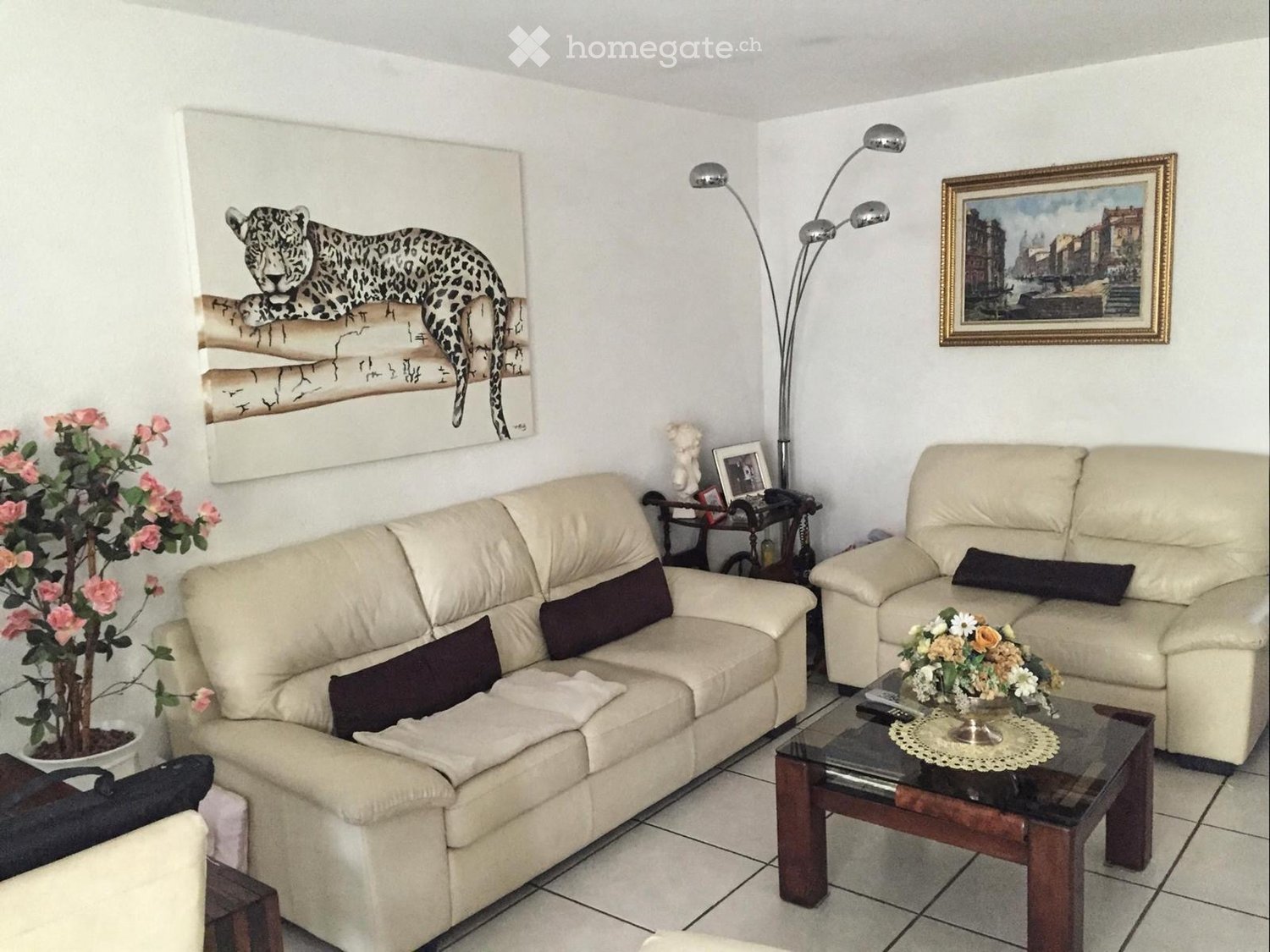 Living room with beige sofas, a glass coffee table, side table, floor lamp, and decorative artwork.