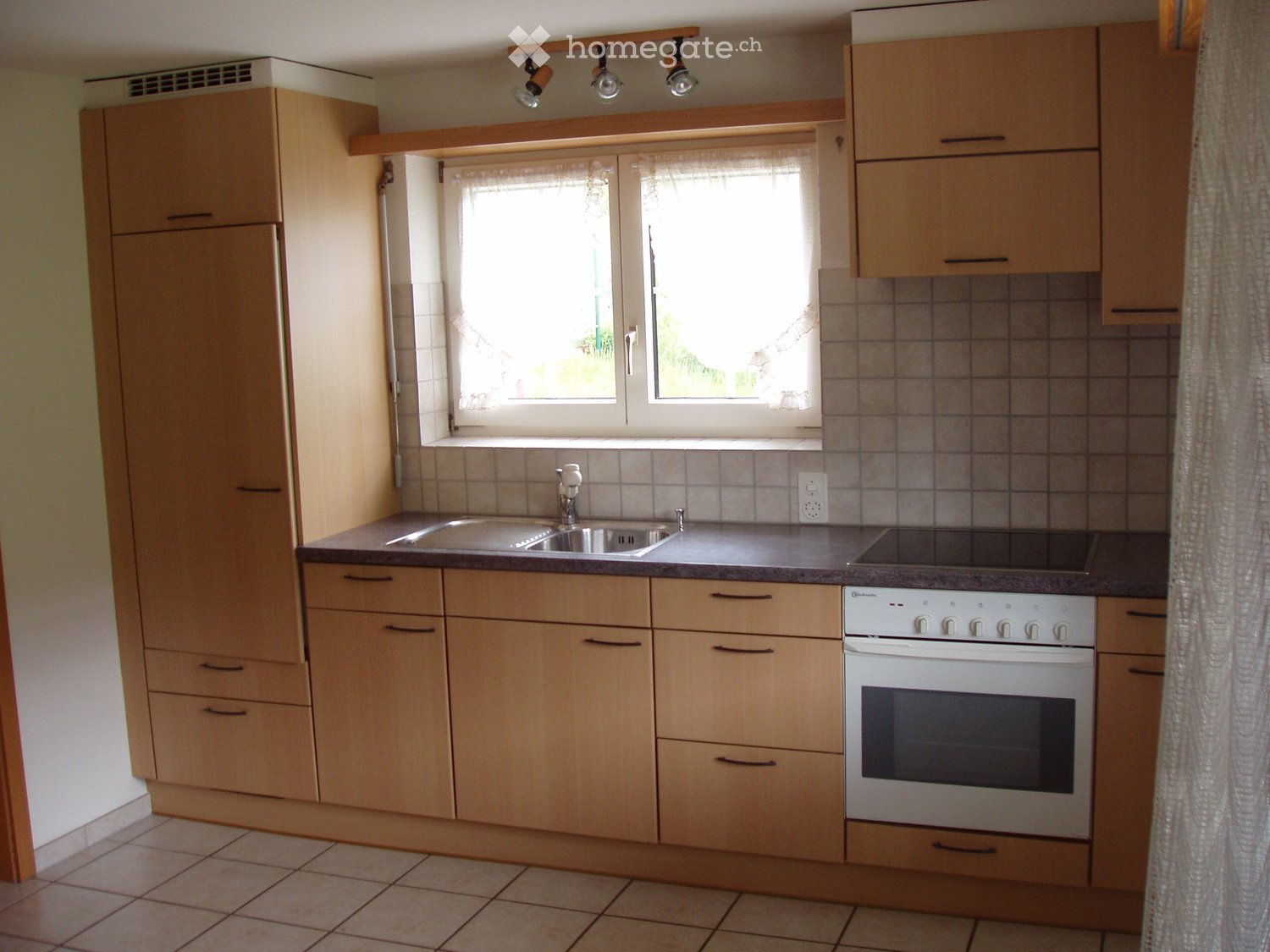Bright kitchen with light wooden cabinets, a sink, a stove, and a window with blinds.