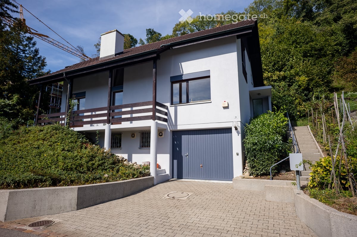 Two-story modern house with white exterior, grey garage door, and raised ground floor accessed by stairs.