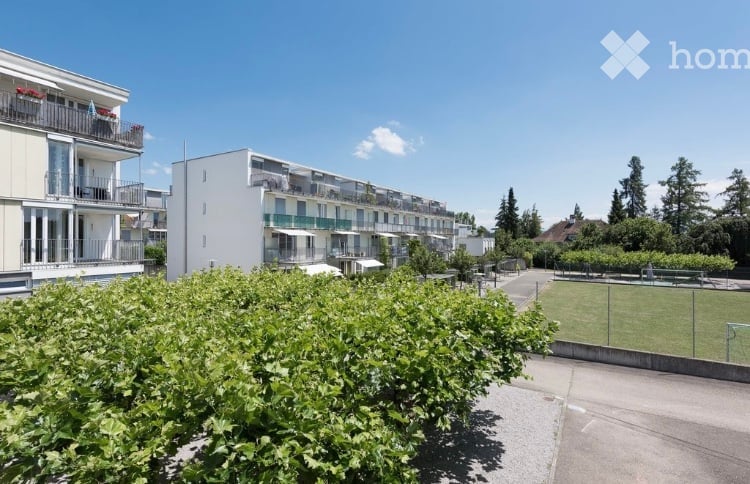 Modern multi-story residential building with balconies and surrounding greenery.