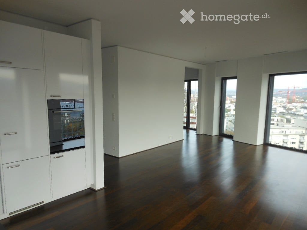 Modern kitchen with dark wooden flooring, white cabinets, and large windows offering a city view.