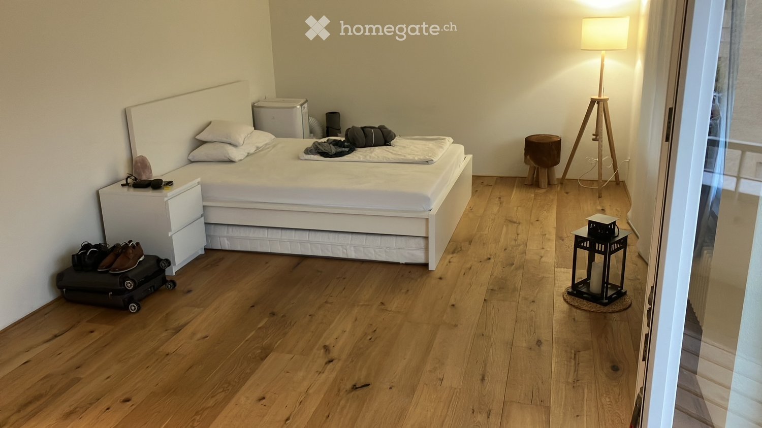 Modern bedroom with a white bed, nightstand, floor lamp, small stool, and decorative lantern on the floor.