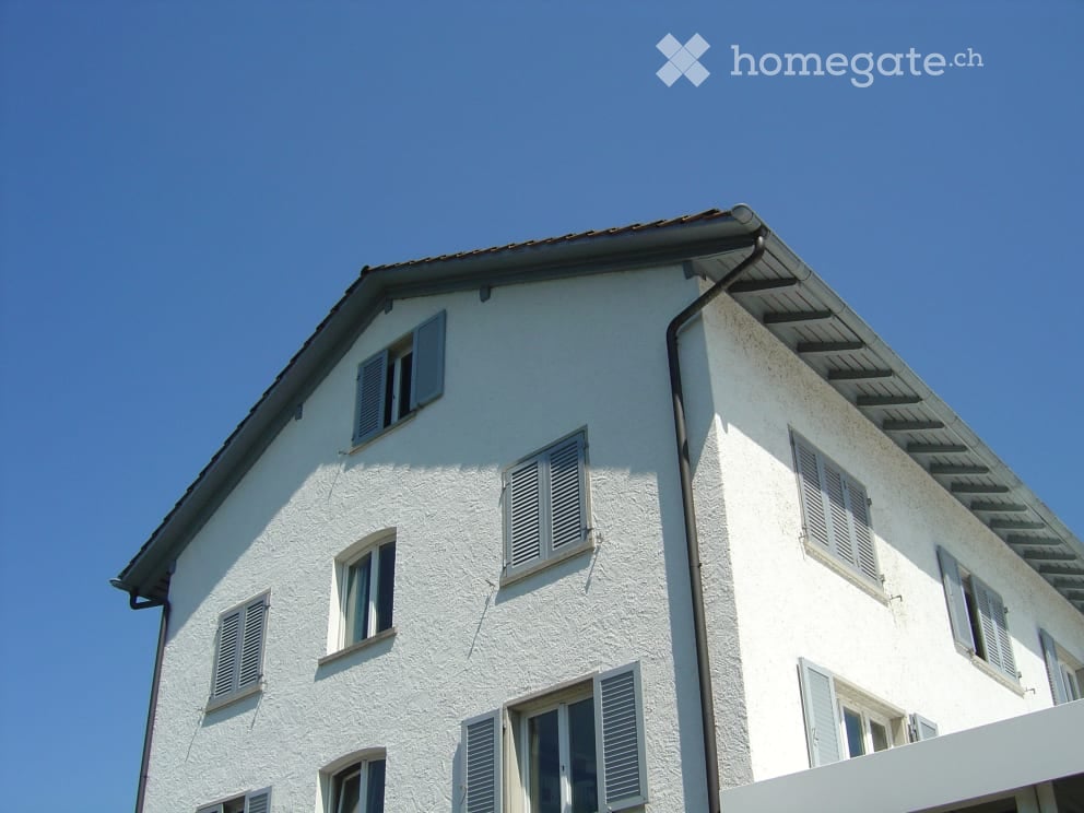 A multi-story white building with multiple windows and shutters under a clear blue sky.