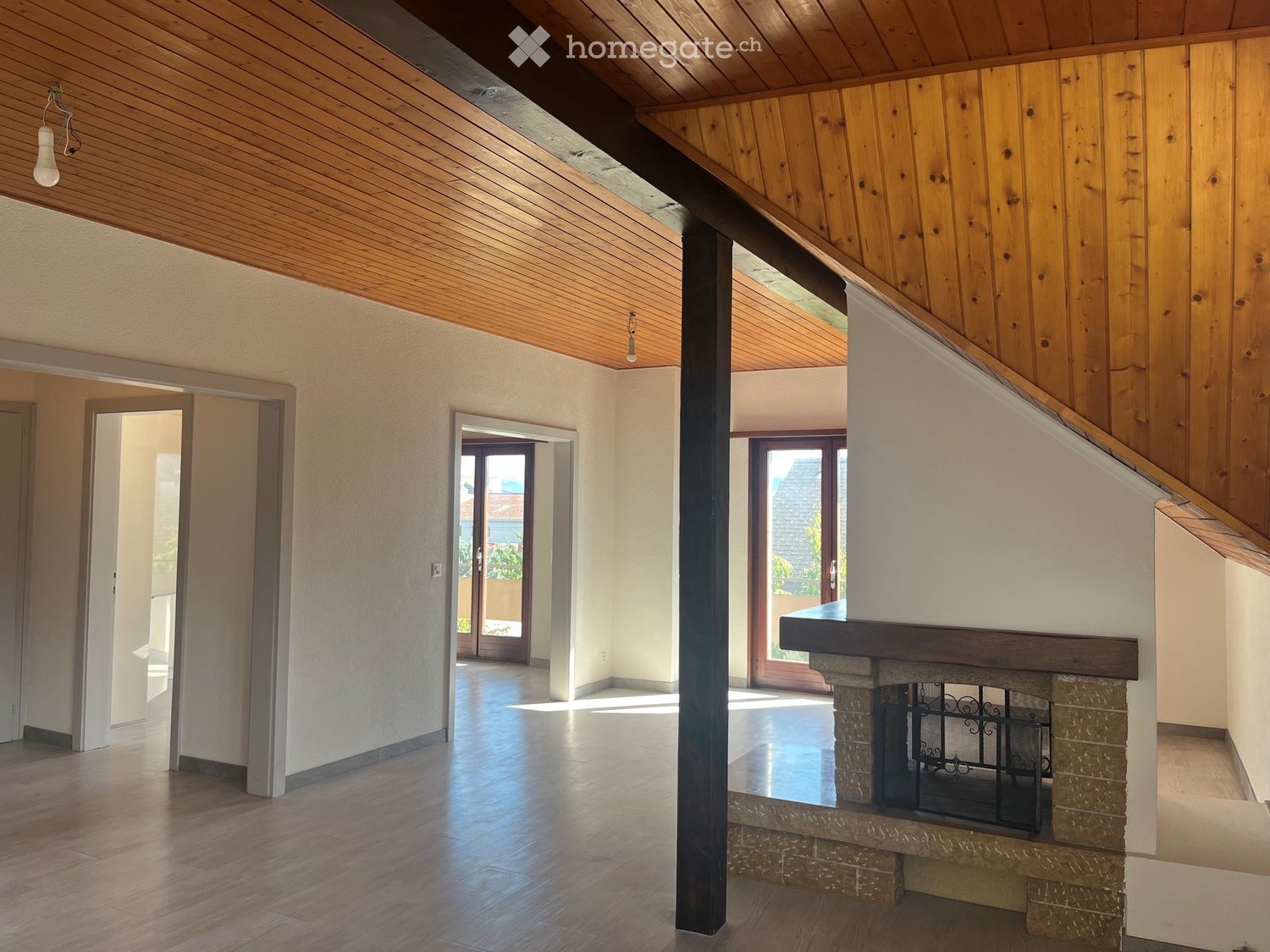 Spacious hallway with wooden ceiling, polished wooden floor, and a stone fireplace with a decorative metal screen. Multiple doorways lead to other rooms.