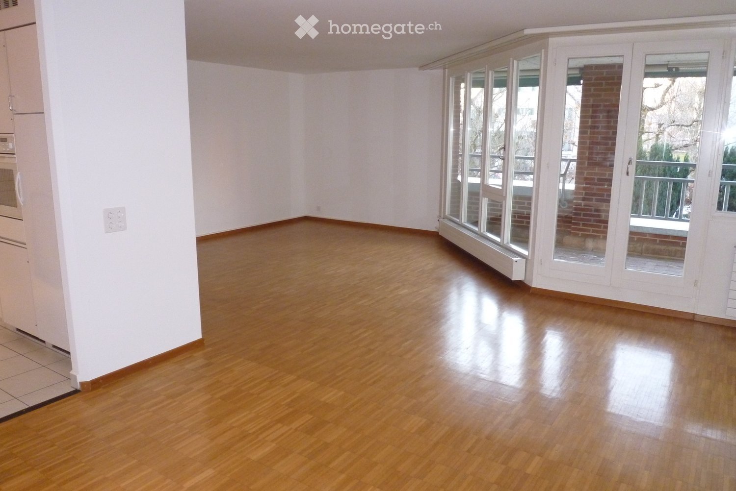 Empty room with polished hardwood flooring, white walls, and large glass sliding doors leading to an outdoor area.