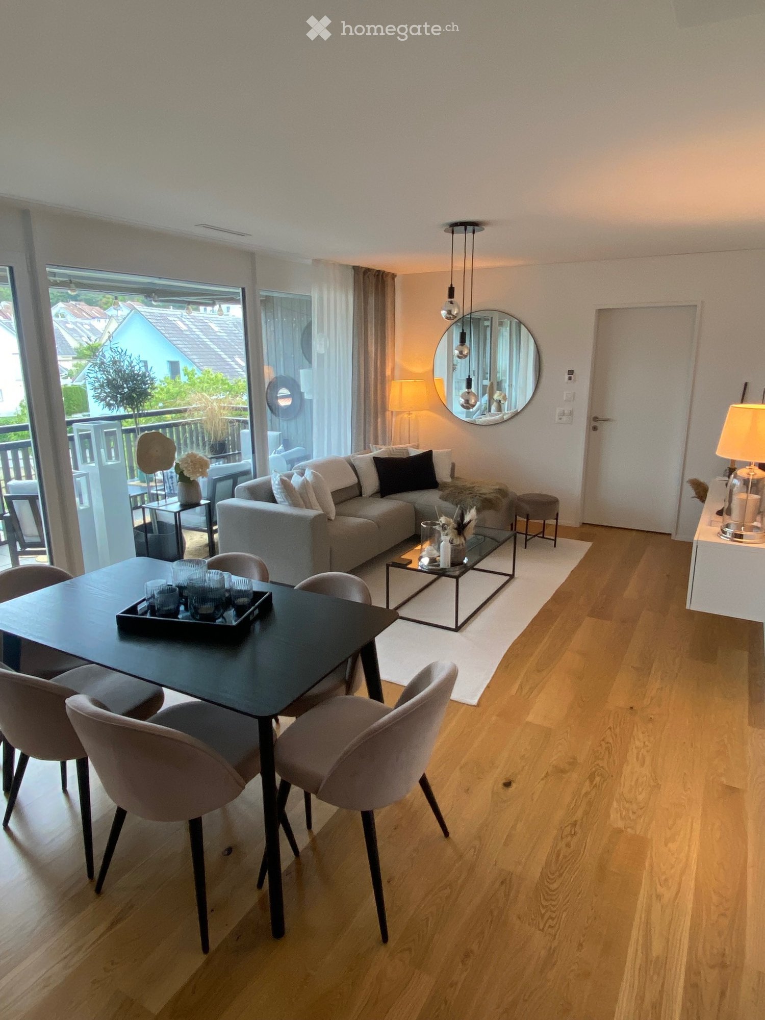 Modern living and dining area with a grey sofa, coffee table, dining table with chairs, and a balcony view.