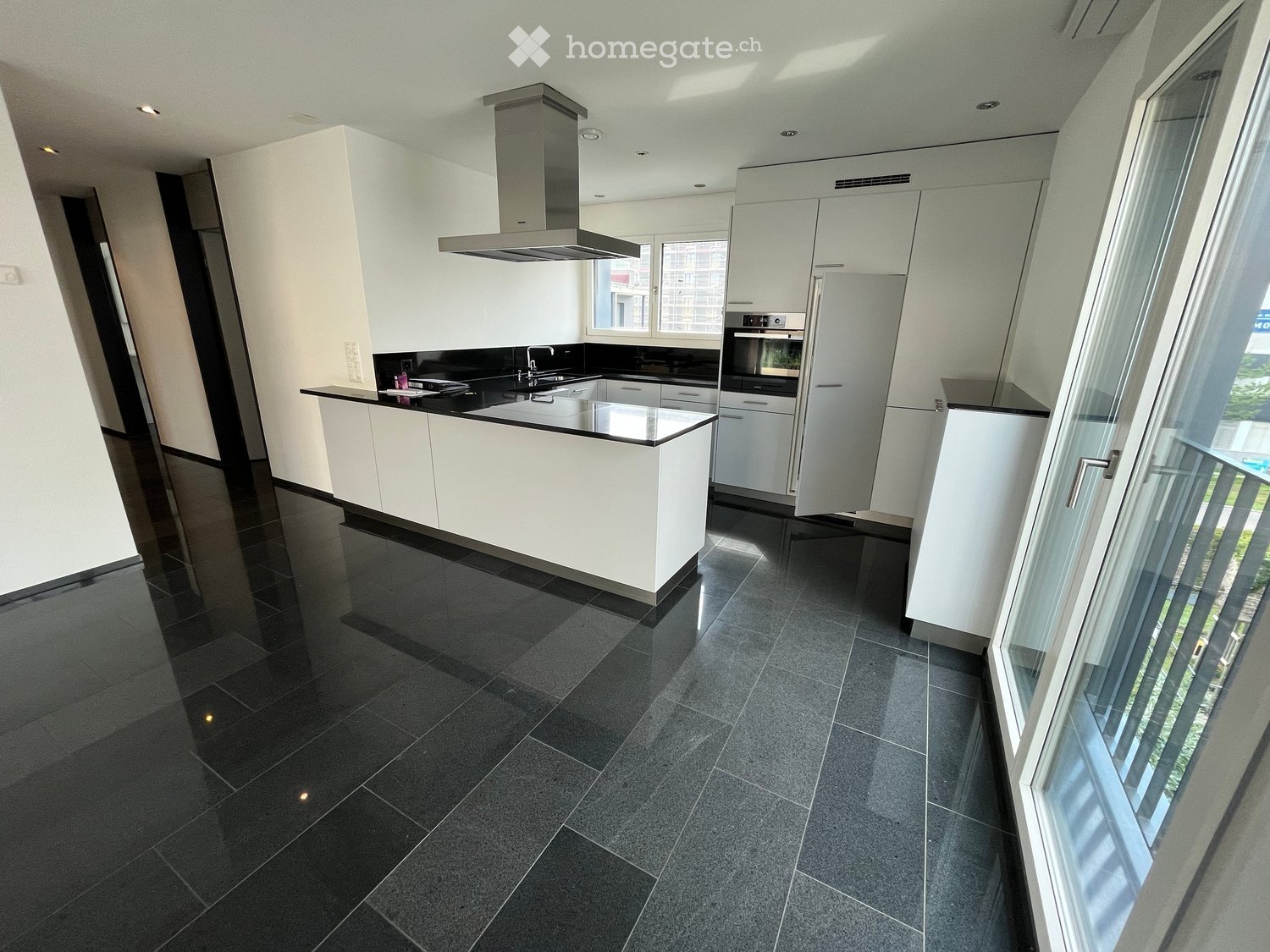 Modern kitchen with white cabinets, black countertops, stainless steel appliances, and a large island.