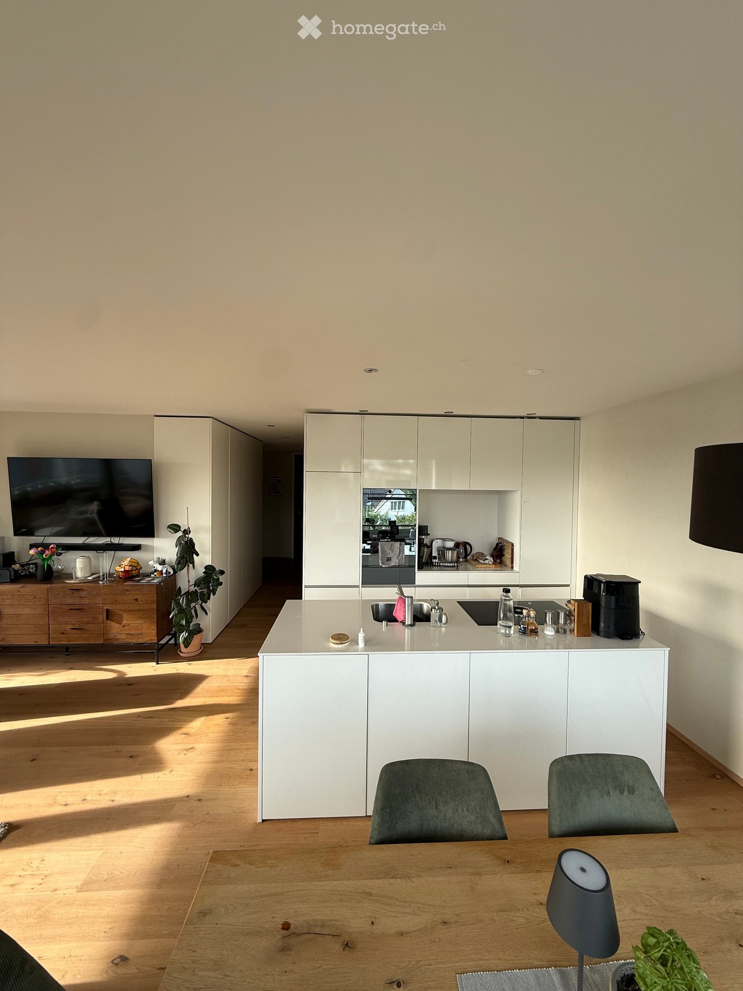 Modern kitchen with white cabinets, wooden floor, island, sink, and seating area with table and chairs.