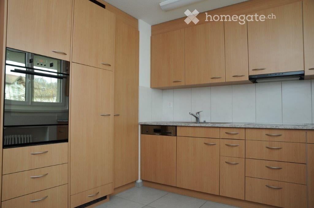Modern kitchen with light wooden cabinets, granite countertop, stainless steel sink, and built-in oven.