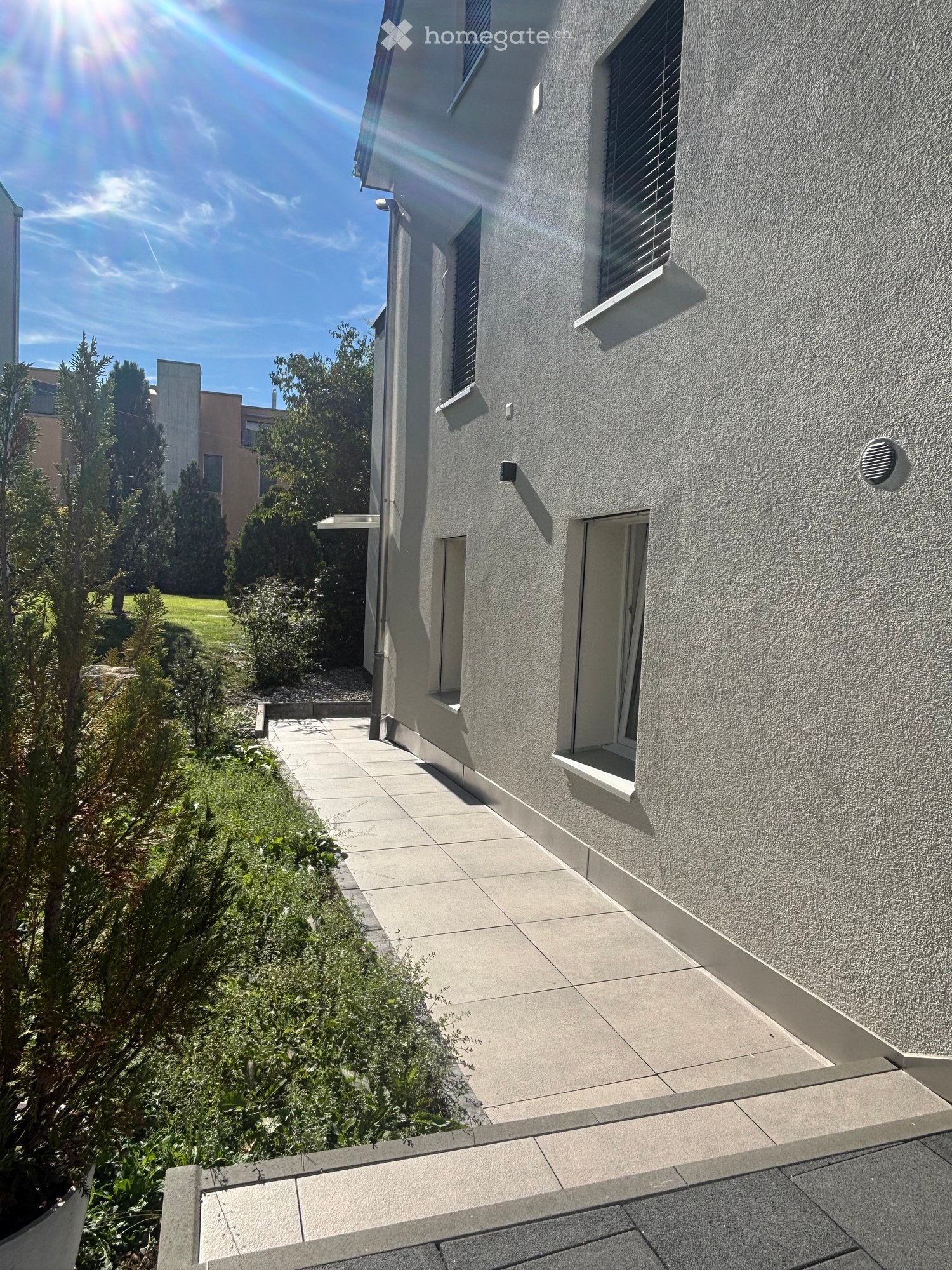 Modern grey building exterior with raised ground floor, small garden, and pathway.