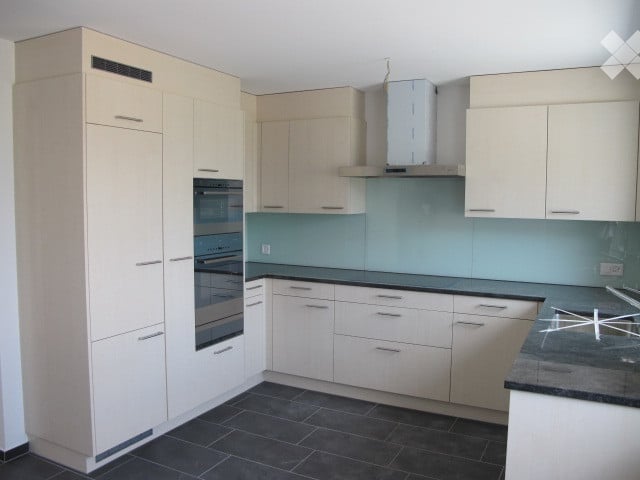 Modern kitchen with white cabinets, stainless steel oven, range hood, and dark countertop.