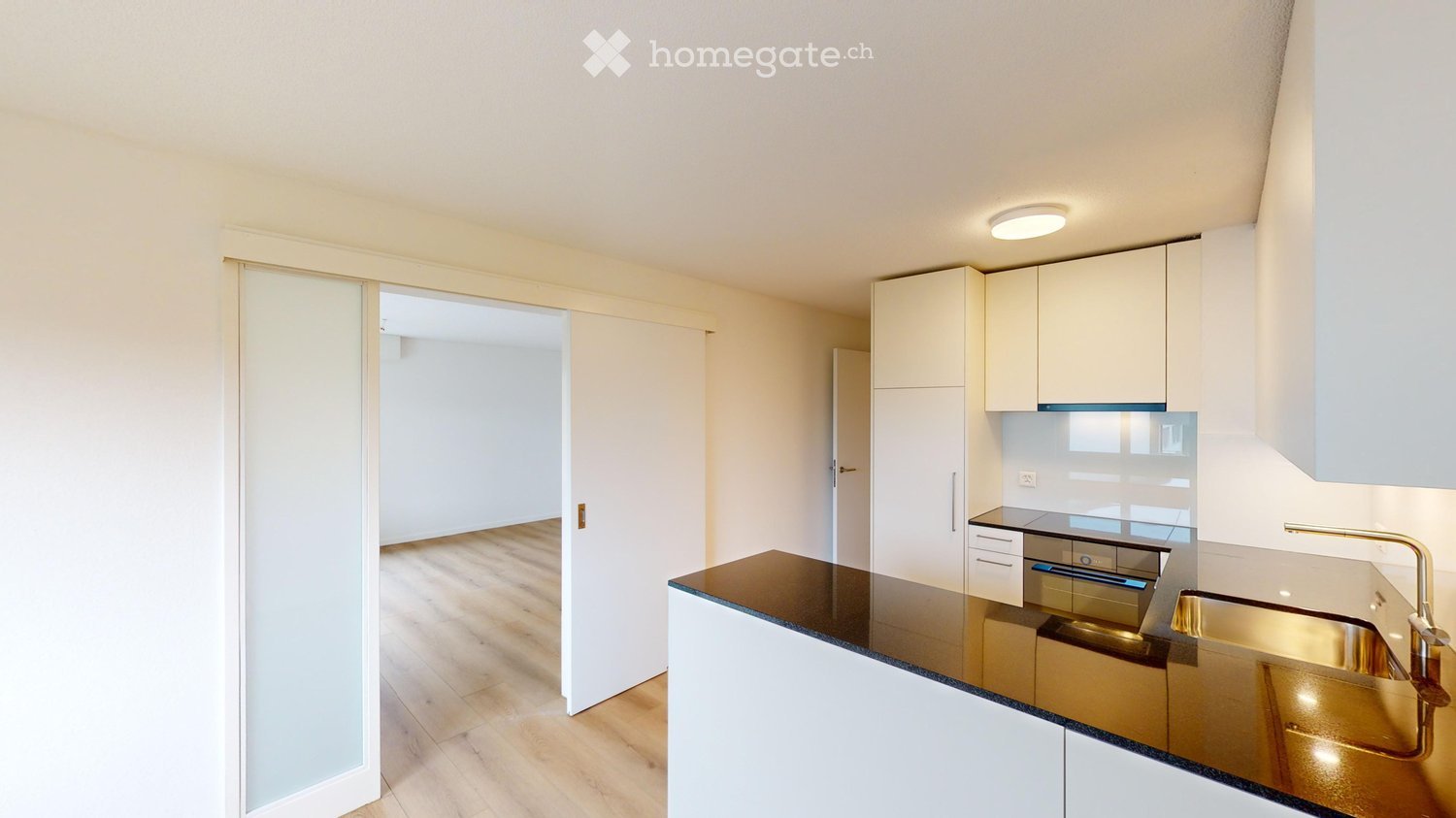 Modern kitchen with white cabinets, black countertop, and a gold sink. The space features wooden flooring and recessed lighting.