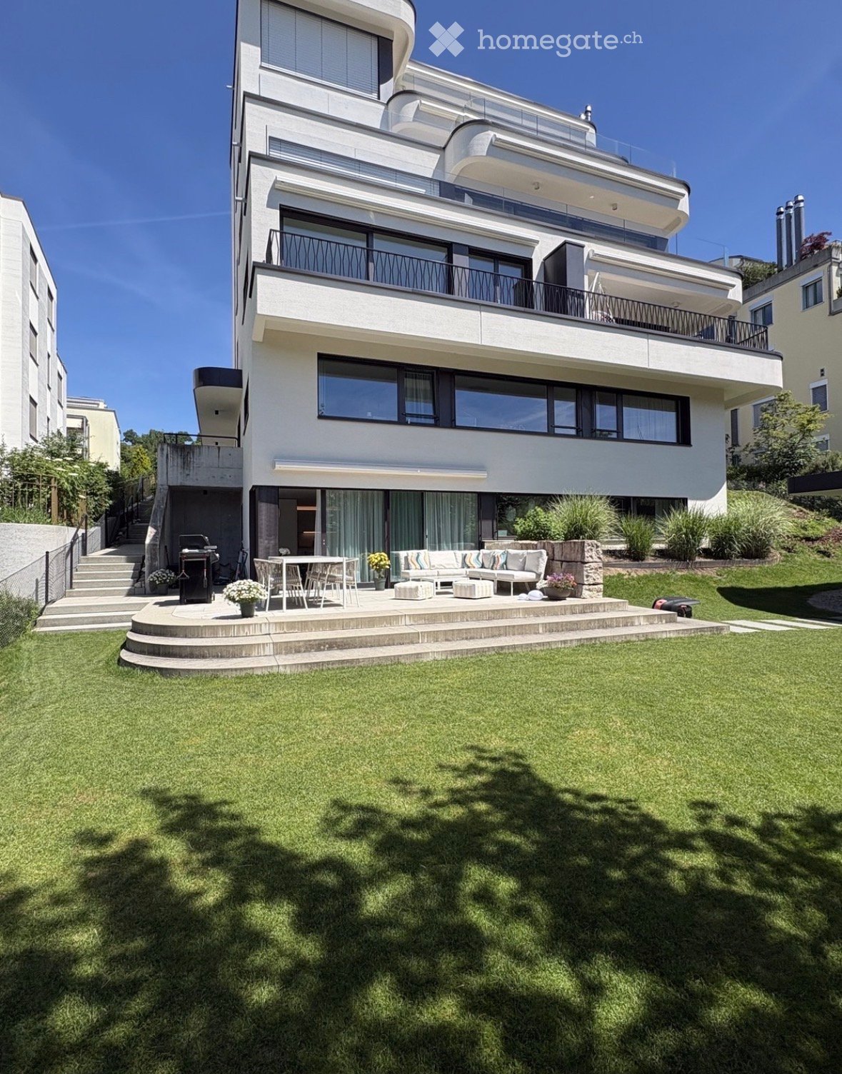 Modern house with a spacious garden and outdoor seating area featuring a sofa, ottomans, a table, and chairs.