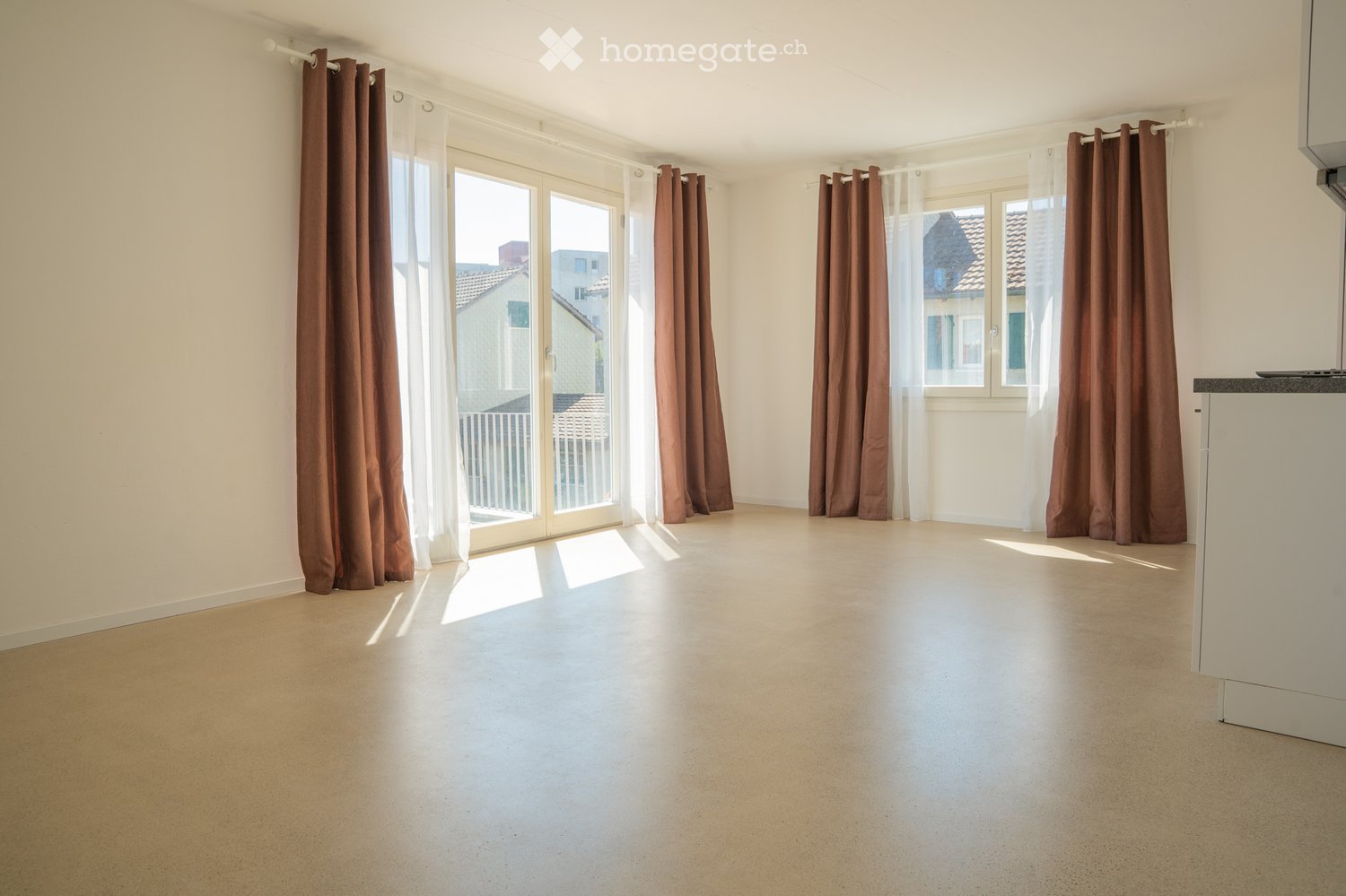 Empty room with beige walls, large sliding glass doors, brown curtains, and a small white cabinet visible on the right side.