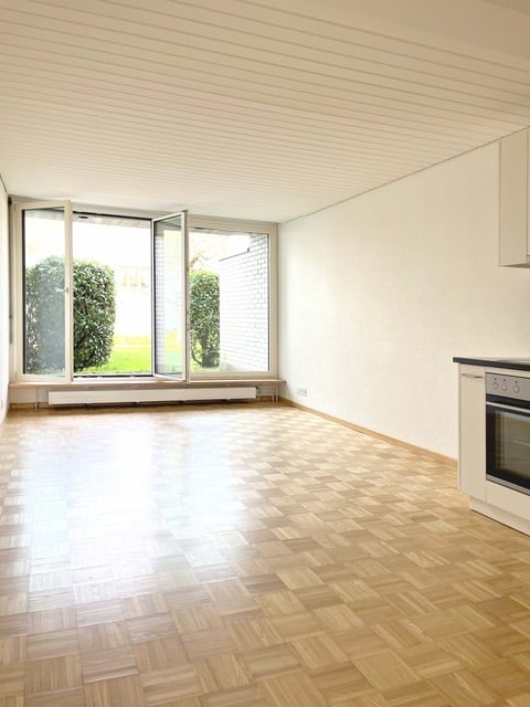 Empty room with wooden flooring, large windows, and white walls. No furniture or equipment present.