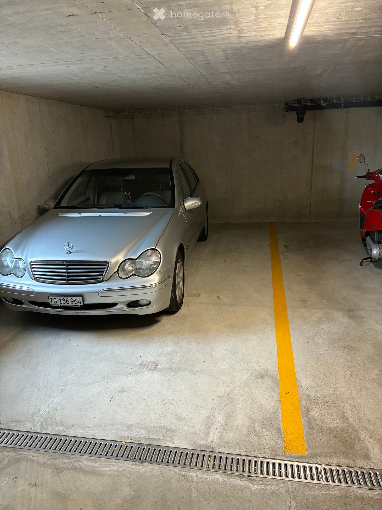 Underground parking garage with a silver Mercedes-Benz car and a red scooter parked inside.