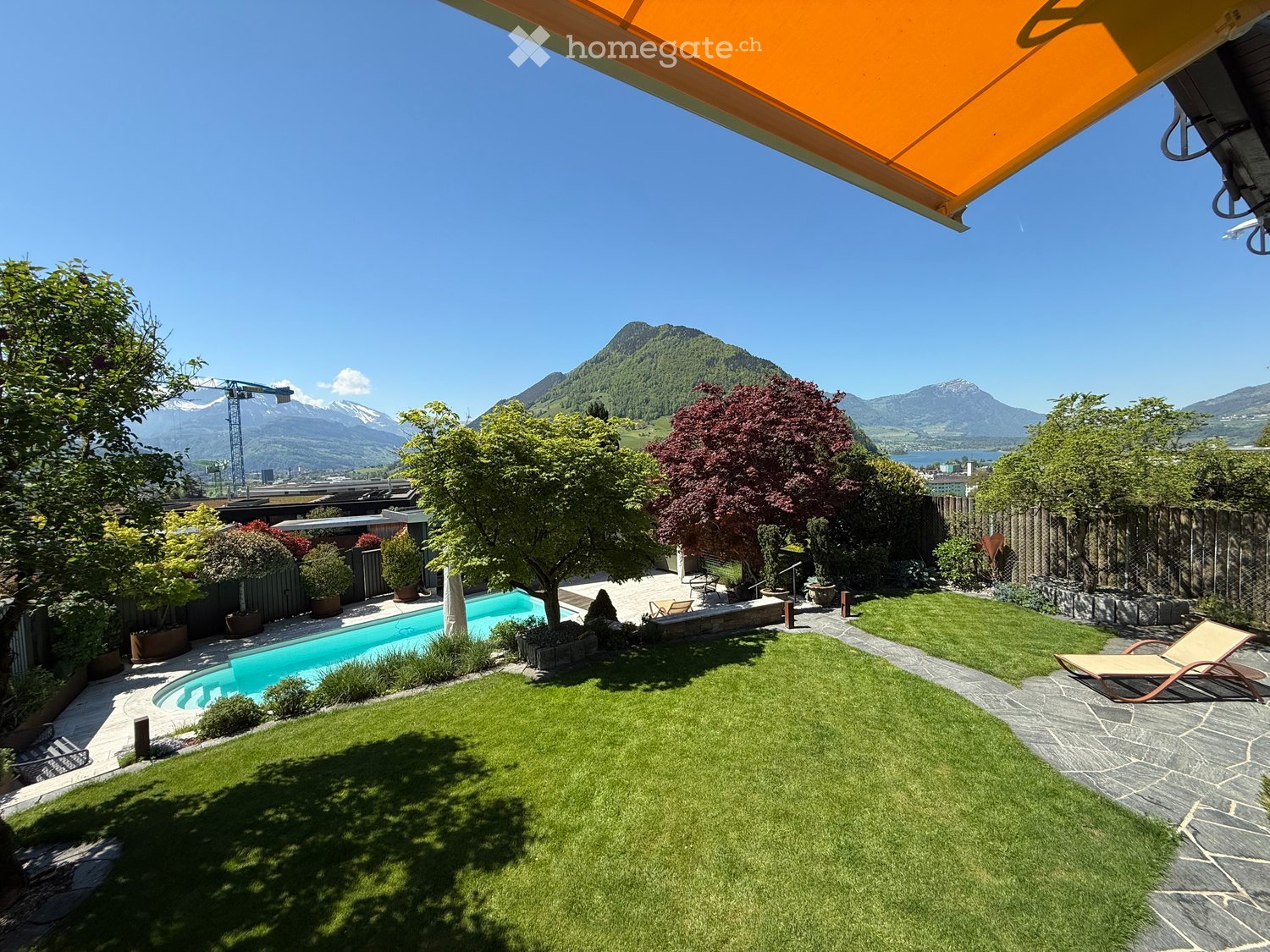 Well-maintained garden with a swimming pool, lounge chairs, and a scenic mountain view in the background.