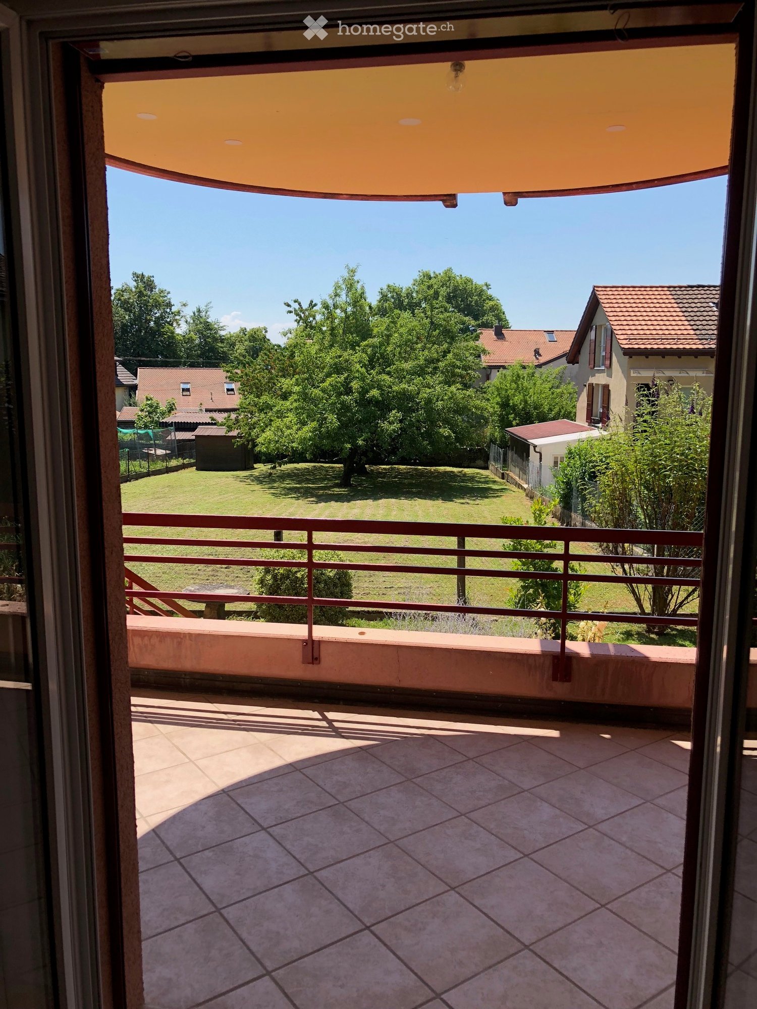 Balcony with tiled floor, metal railing, and a view of a green lawn and neighboring houses.