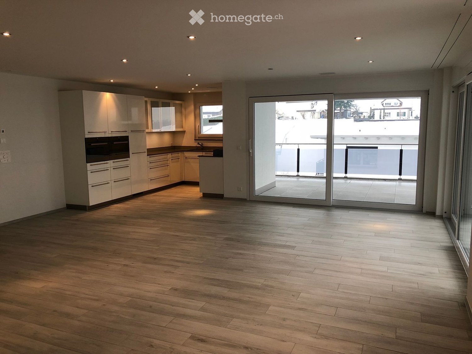 Empty kitchen with light wood flooring, white cabinetry, and large sliding glass doors leading to a balcony.