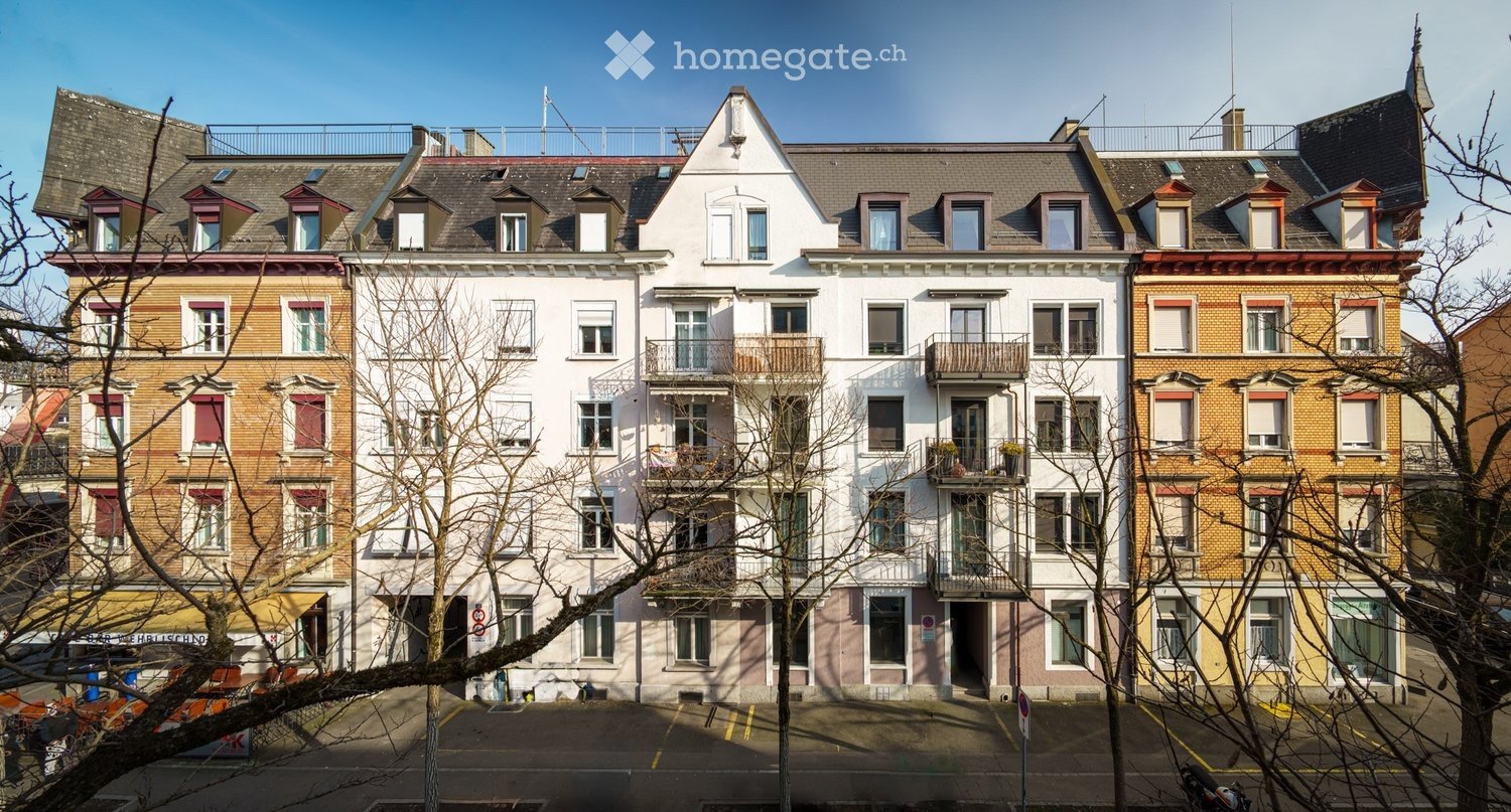 A row of multi-story residential buildings with varied facades, featuring balconies, windows, and a mix of architectural styles.