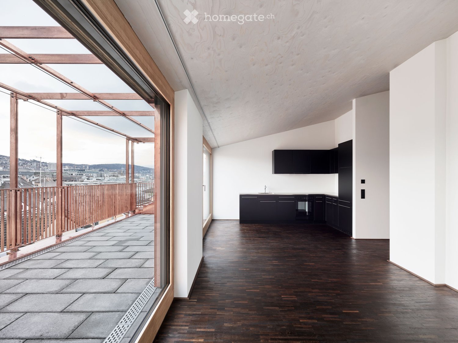 Modern kitchen with dark cabinets, wooden flooring, and a large window opening to a balcony area with wooden railings and tiled flooring.