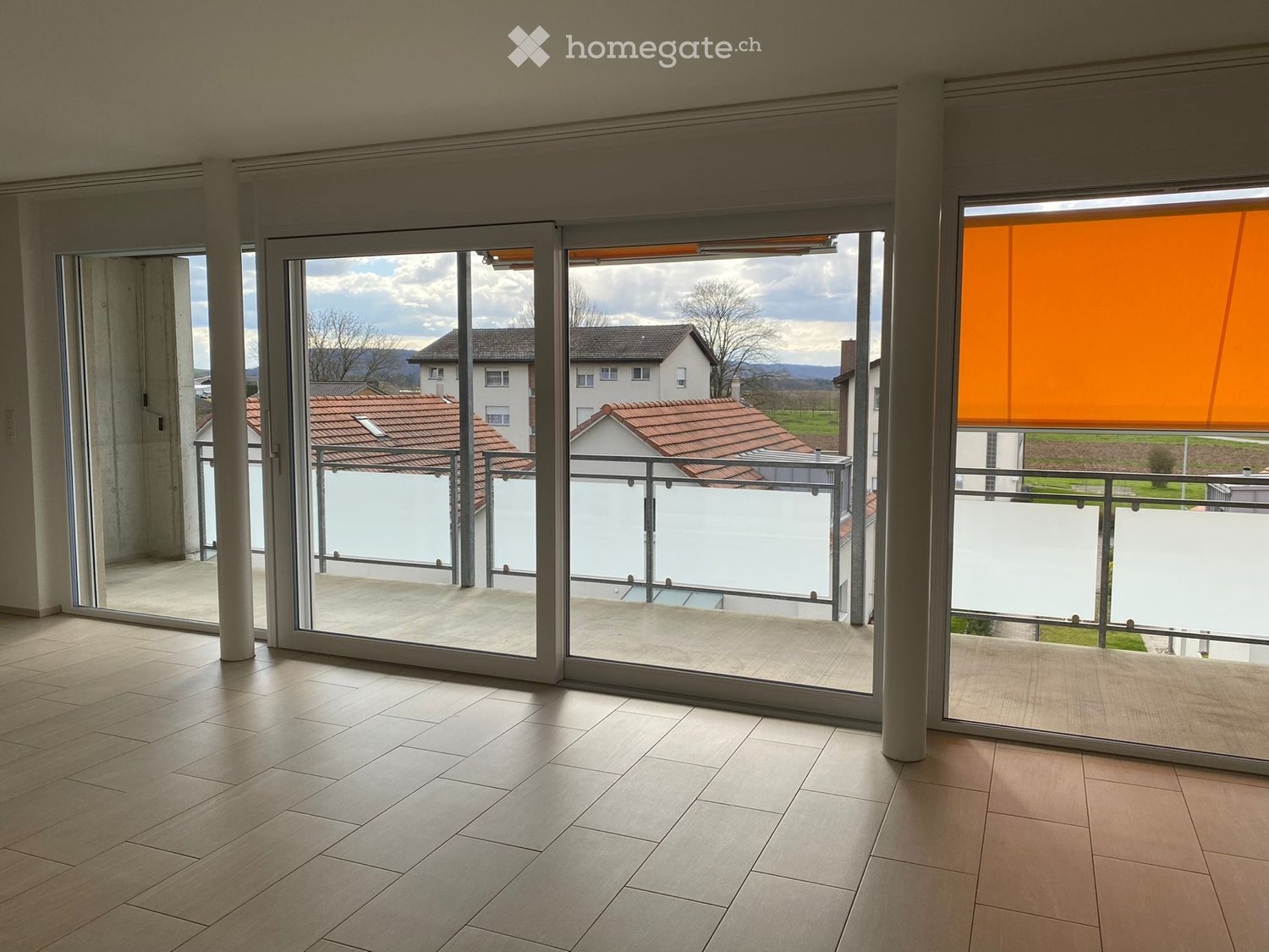 Empty room with large sliding glass doors leading to a balcony, tiled floor, and modern interior design.