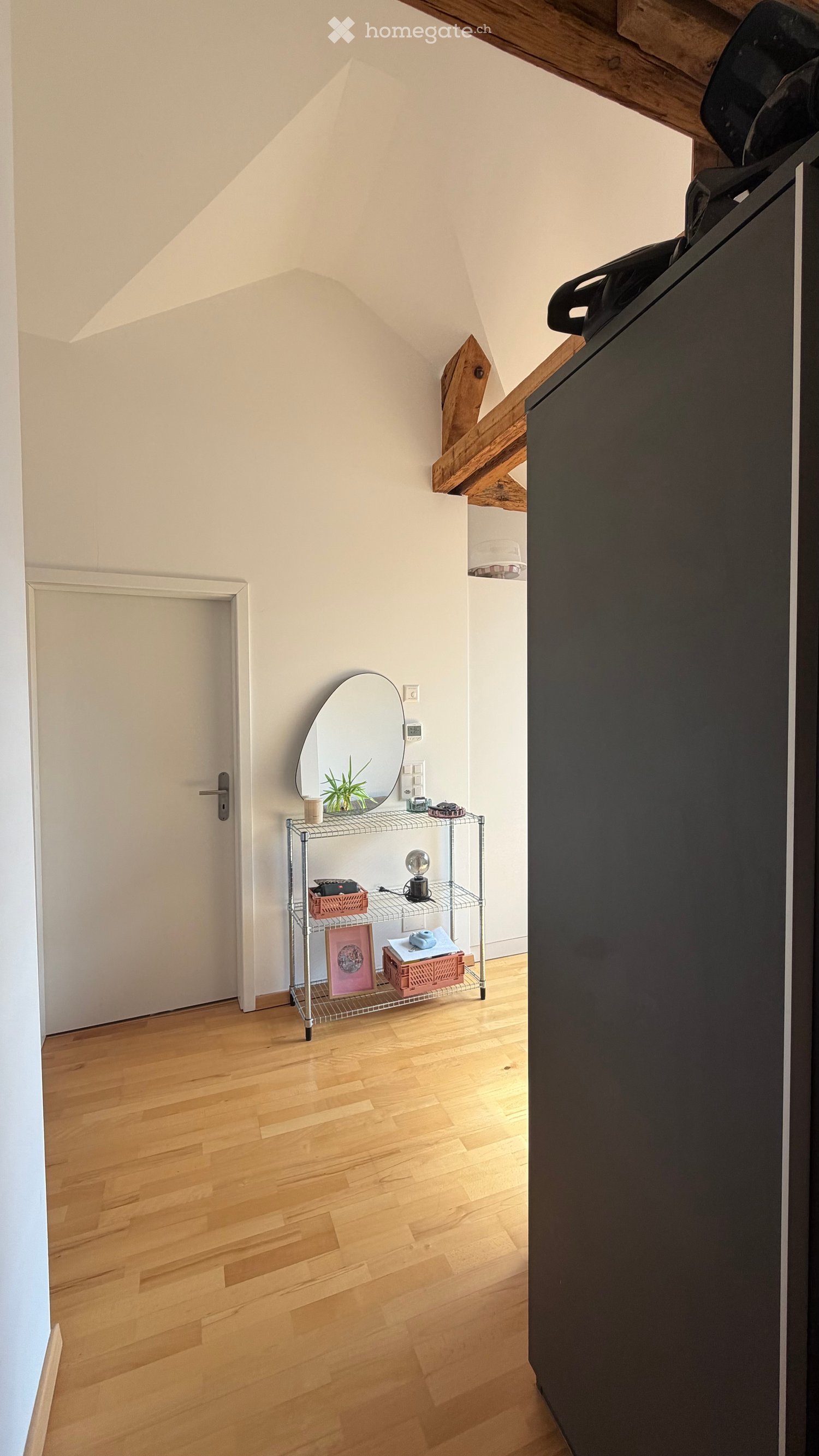 Attic room with wooden flooring, slanted ceiling, and a small shelf holding a mirror, lamp, plant, and picture frame.