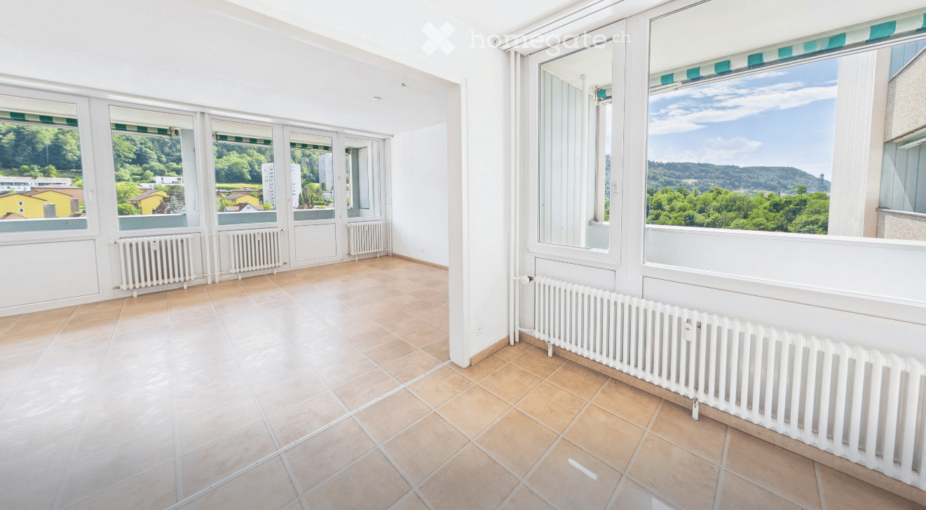Bright, empty room with large windows offering scenic views, tiled floor, and white radiators.