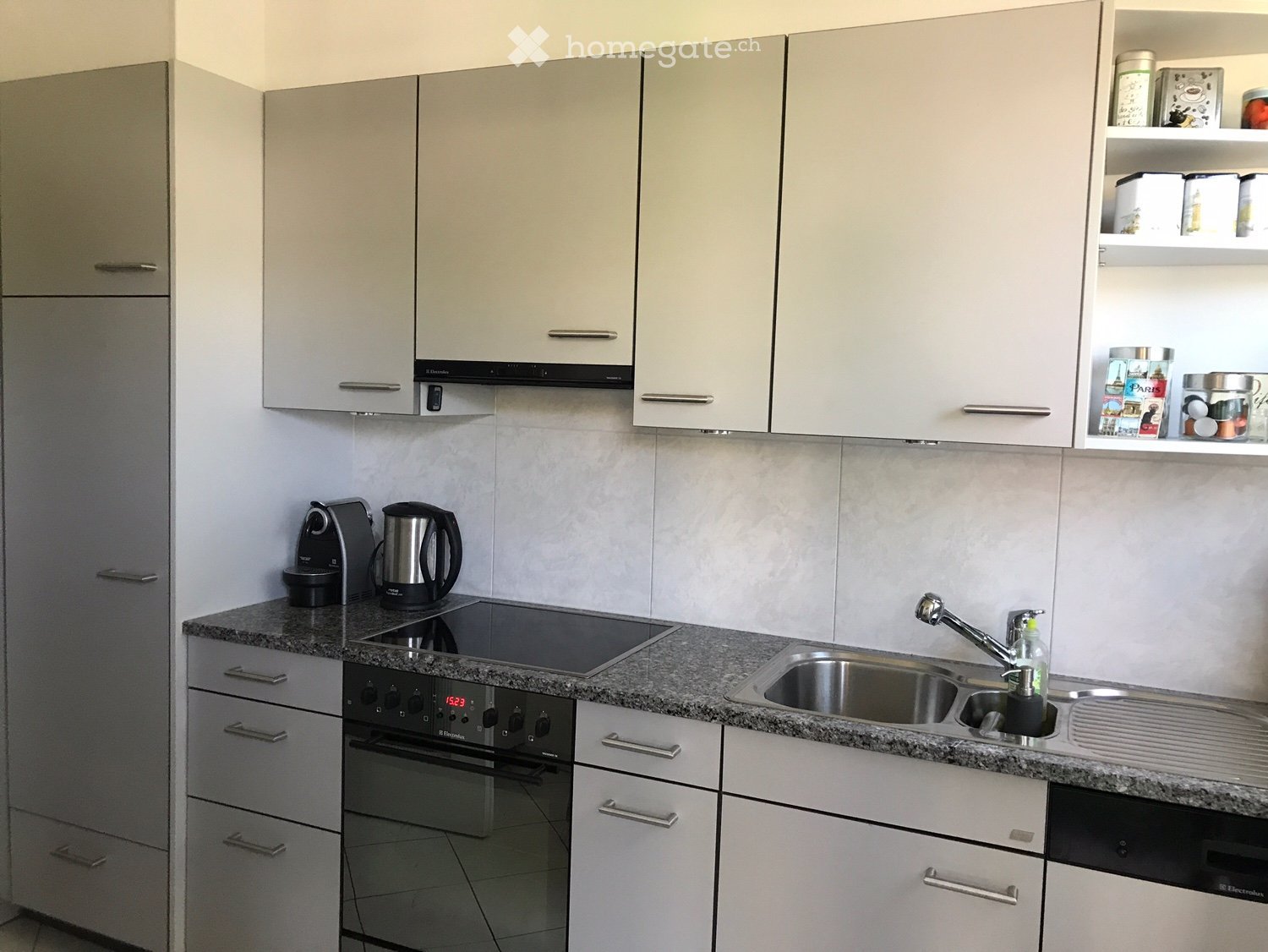 Modern kitchen with white cabinets, granite countertop, stainless steel sink, electric kettle, coffee maker, and built-in oven.