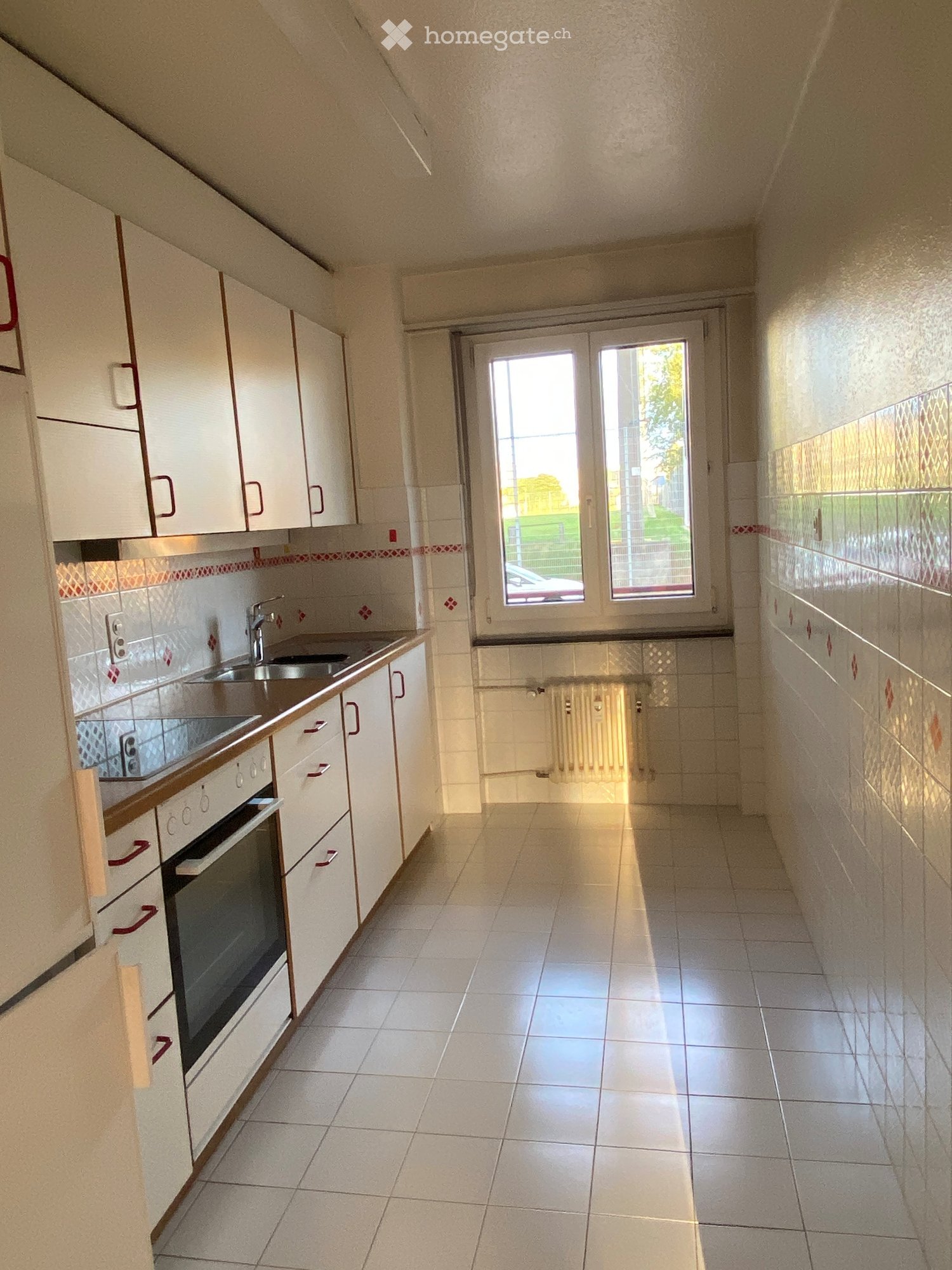 Modern kitchen with white cabinets, tiled walls, and a large window. Features a sink, oven, and faucet.