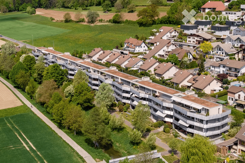 Aerial view of a residential area with multiple apartment buildings and houses, surrounded by green fields and trees.