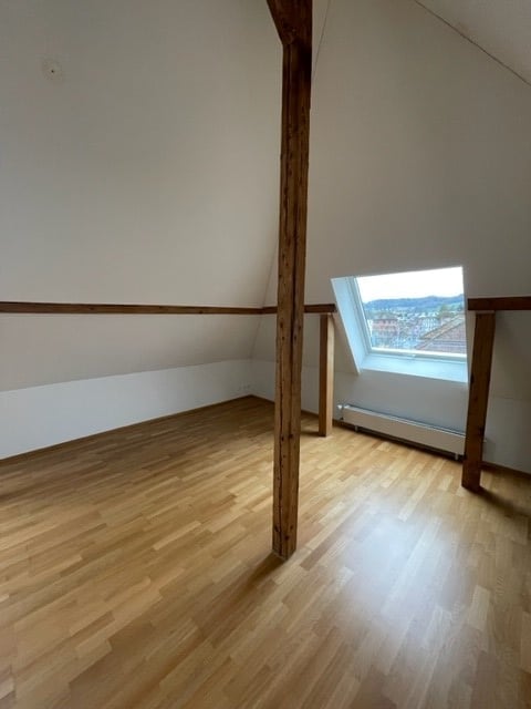 Empty room with wooden flooring, white walls, and a skylight window offering a view.