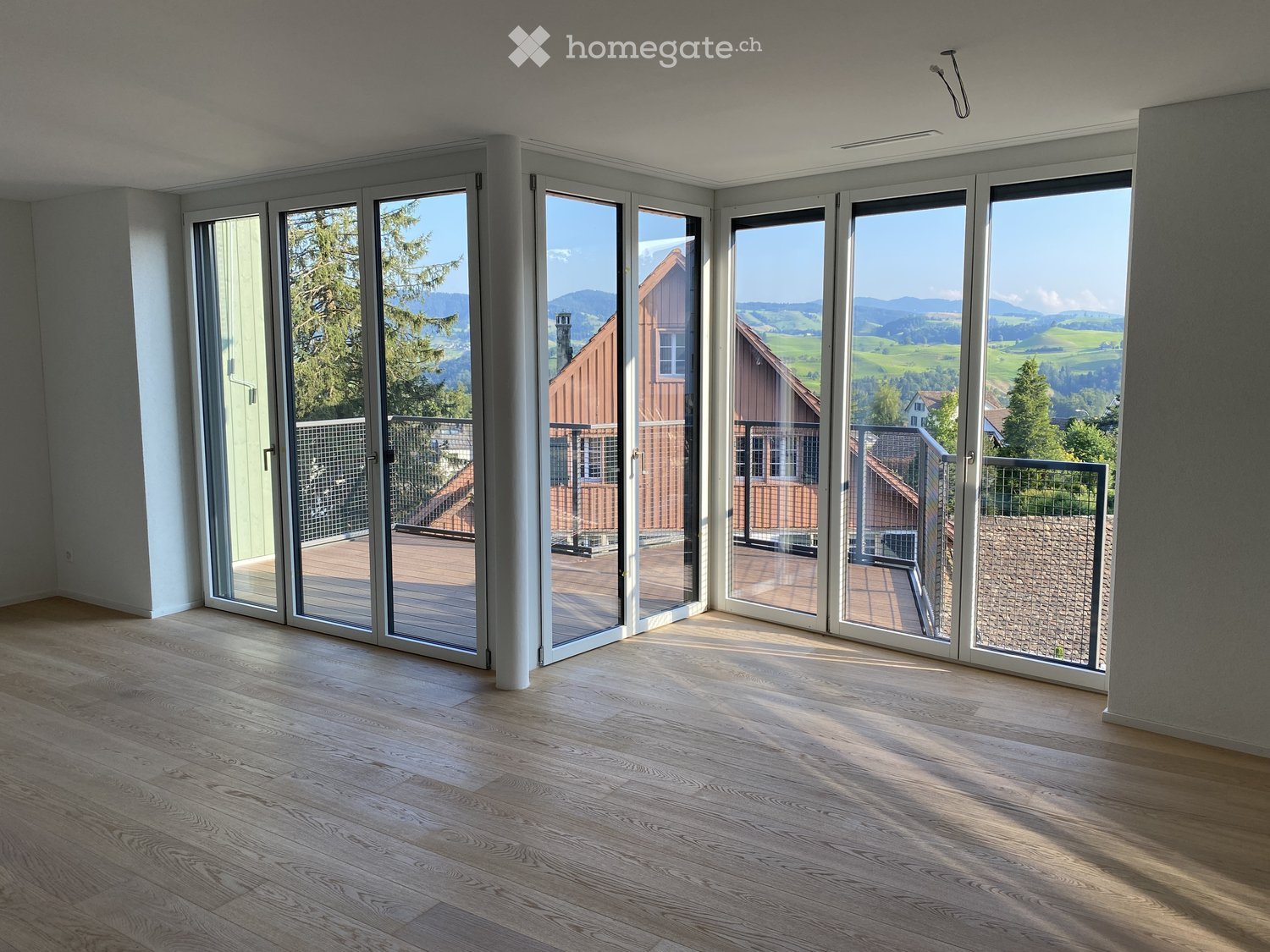 Empty room with large sliding glass doors leading to a balcony, wooden flooring, and a scenic mountain view.