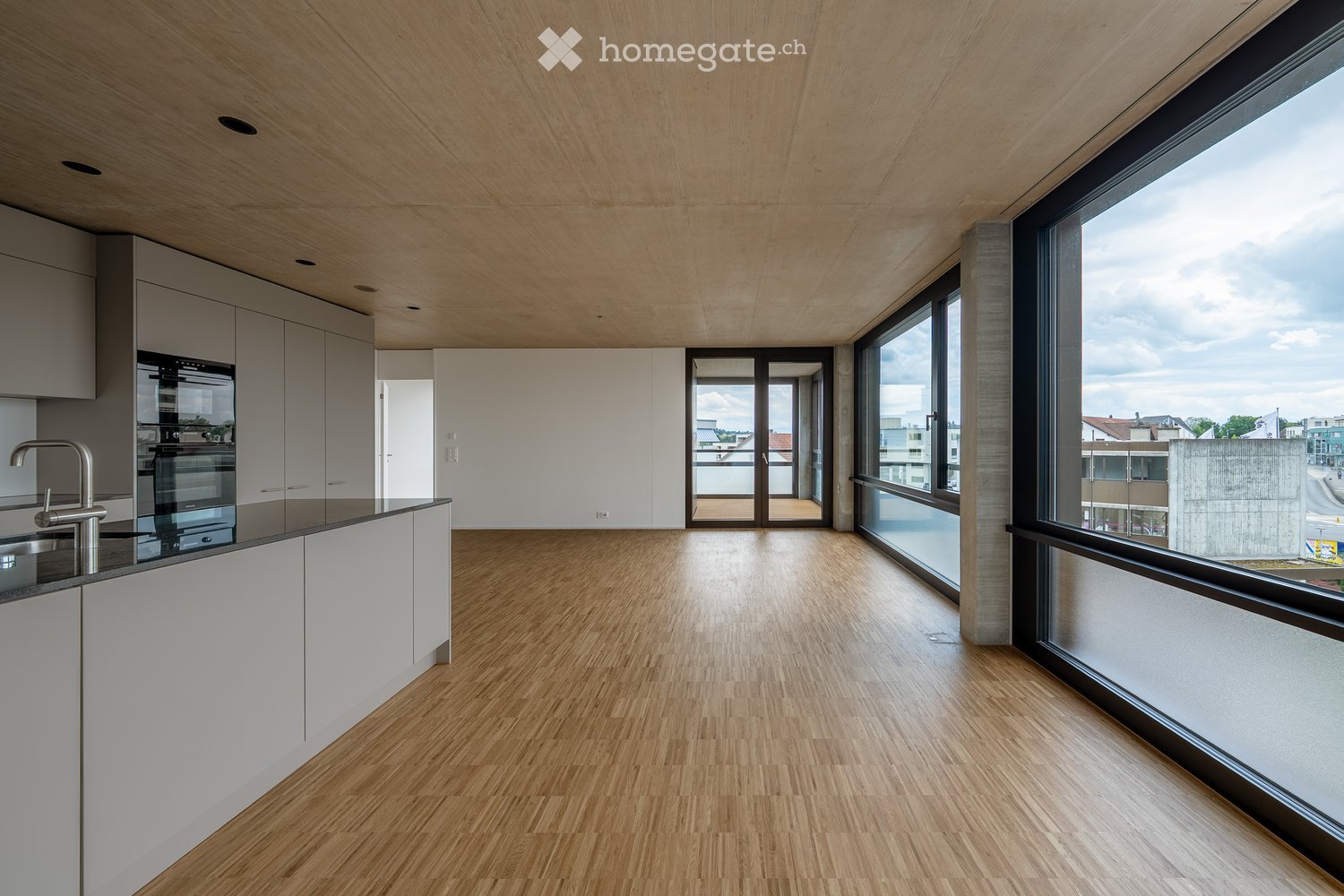 Modern kitchen with light wood flooring, white cabinets, and large windows offering a city view.