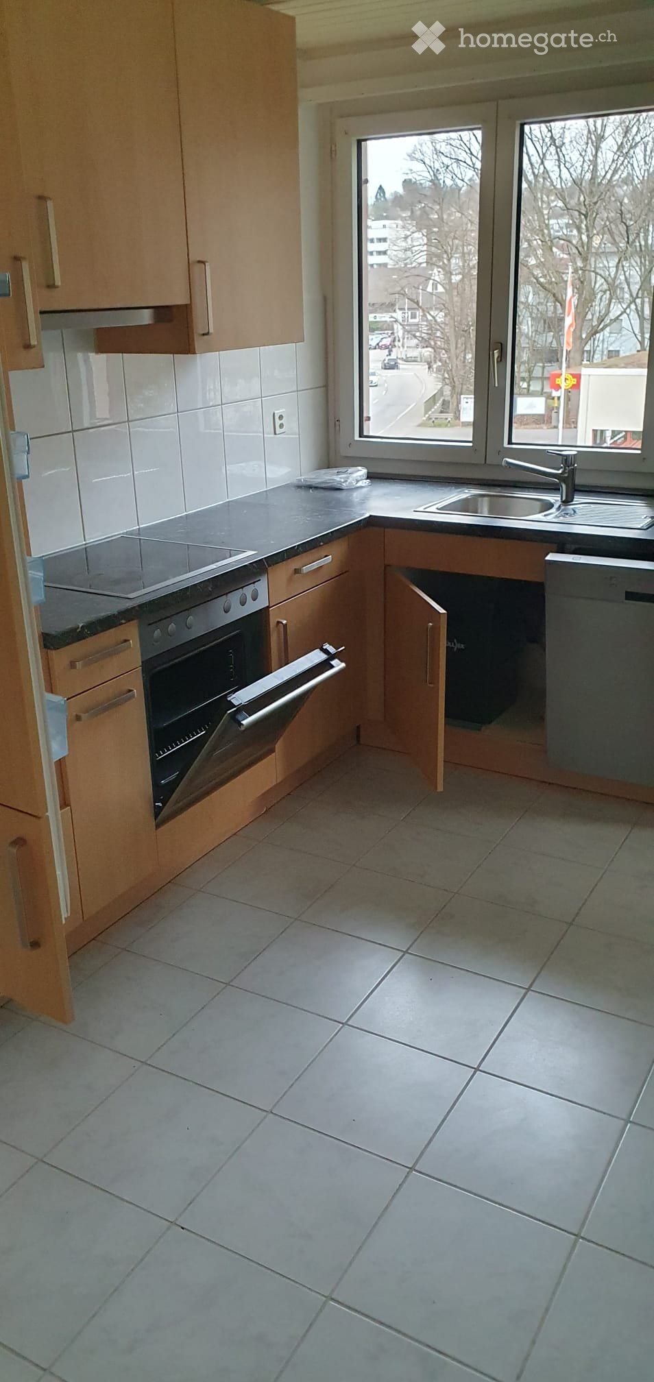 Modern kitchen with light wooden cabinets, tiled walls, and a black countertop. Features an oven, dishwasher, and sink.