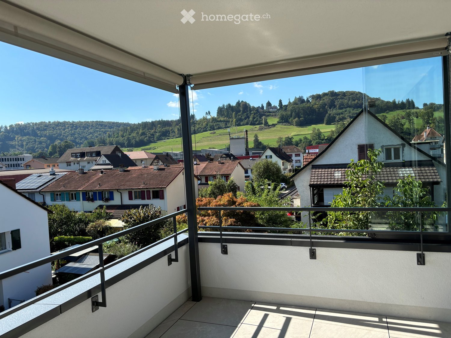 Balcony with glass railings, tiled floor, view of the town and mountains