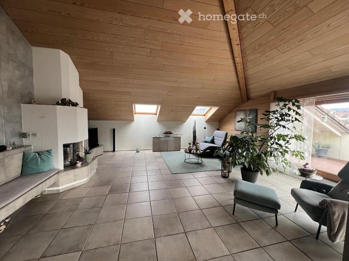 Modern living room with a fireplace, wooden ceiling, large windows, and comfortable seating including a sofa, ottoman, and coffee table.