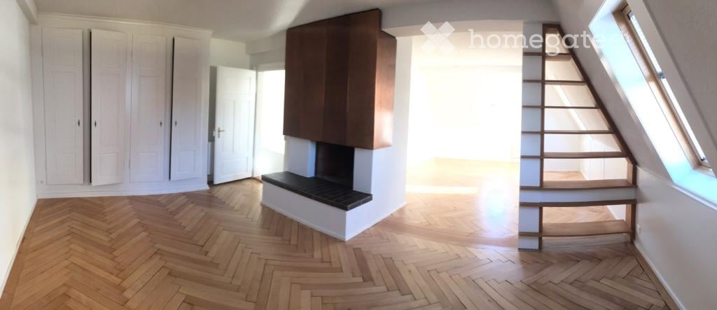 Empty room with wooden herringbone flooring, white walls, built-in cabinetry, and a staircase leading upwards.