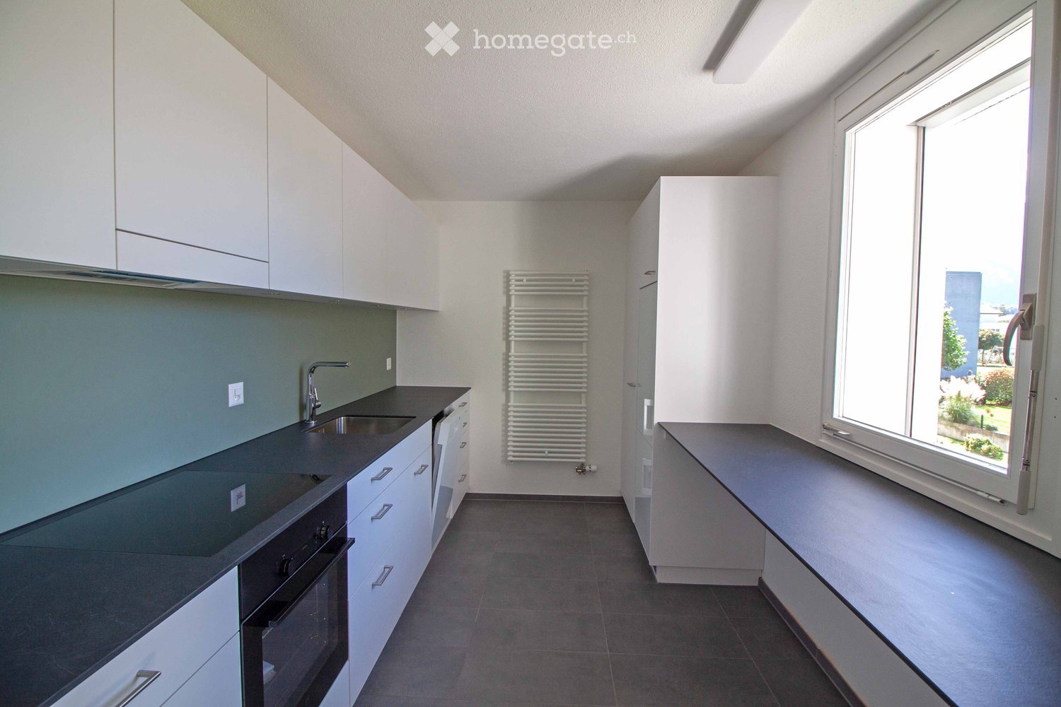 Modern kitchen with white cabinets, dark countertops, sink, faucet, oven, and radiator.