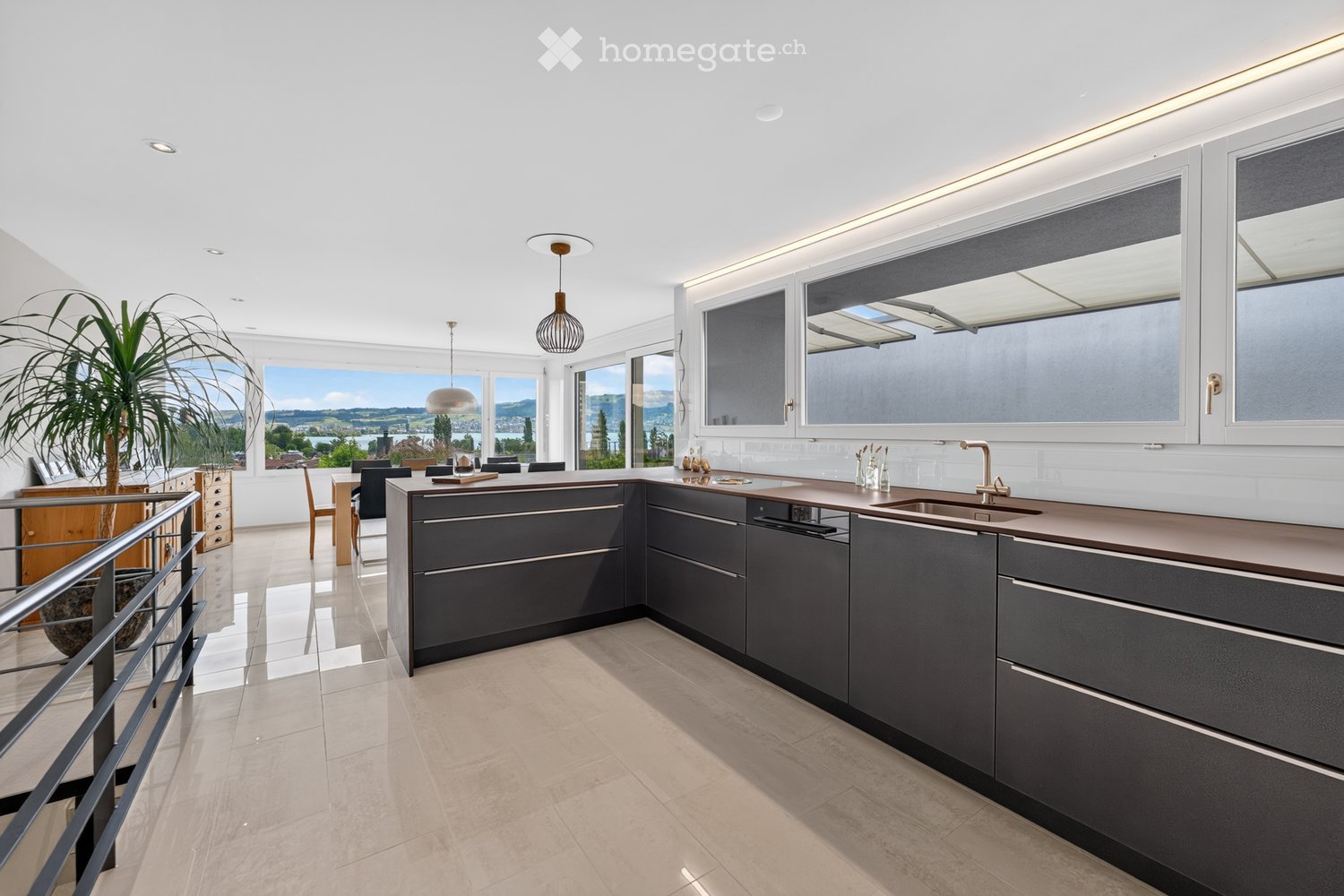 Modern kitchen with grey cabinets, island, sink, and pendant lights. Large windows offer a scenic view of the landscape.