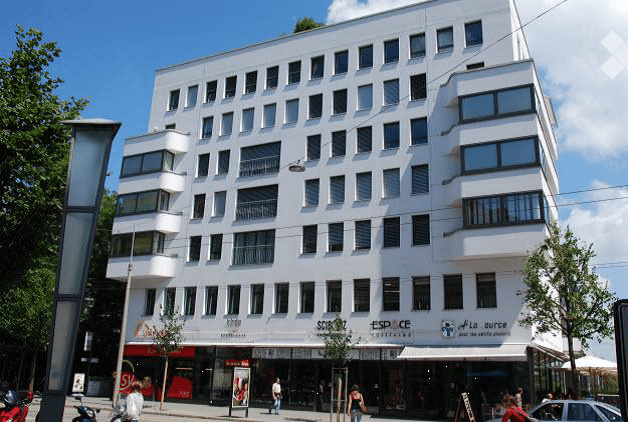 Modern white building with many windows, shops on the ground floor, balconies on upper floors
