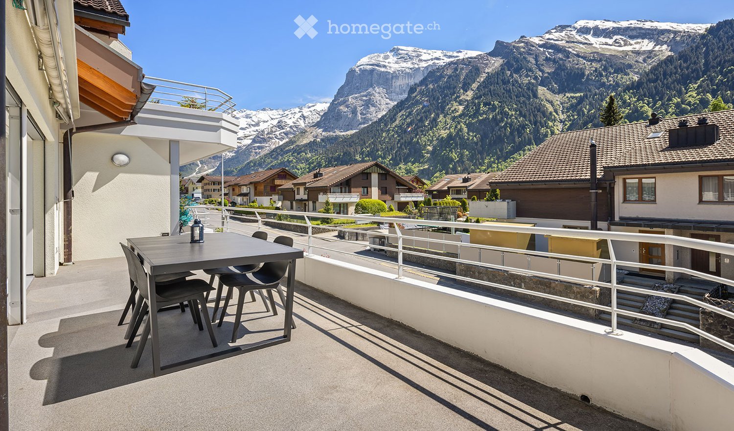 Balcony with a table and chairs, overlooking a scenic mountain view and town.