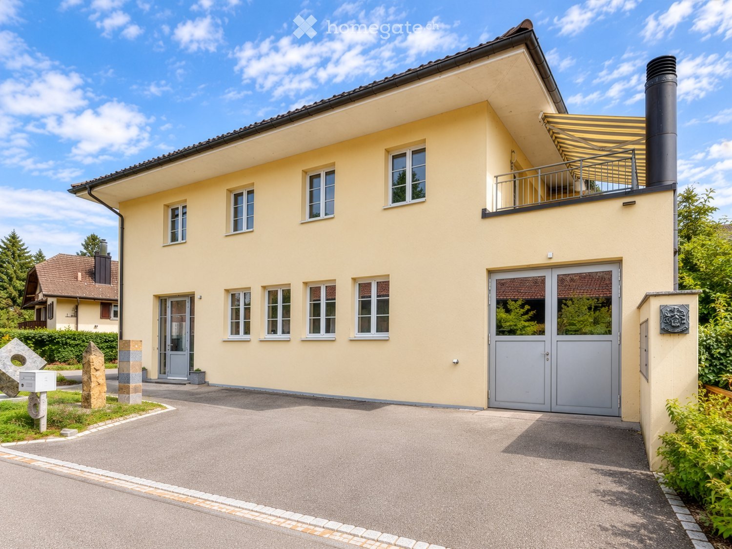 Two-story yellow house with multiple windows, a balcony, and a driveway.