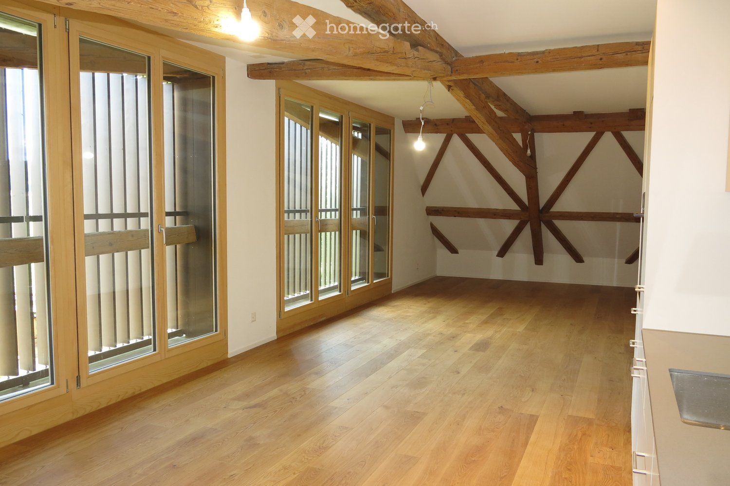 Empty room with wooden flooring, exposed wooden beams on the ceiling, and large glass doors leading to an outdoor area.